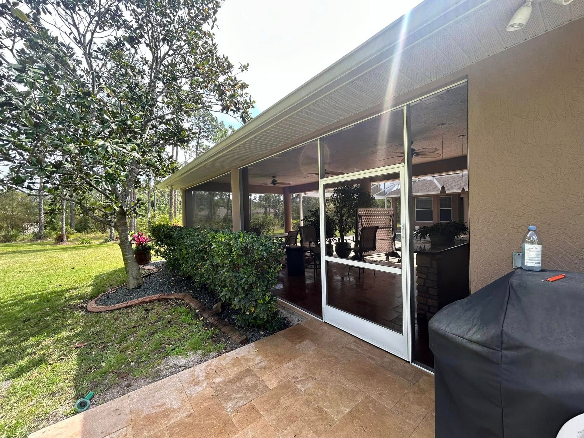 Patio with glass doors, black grill cover, and lawn beside a house under trees