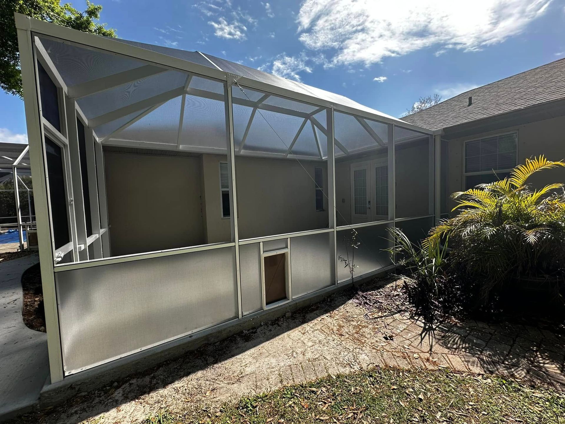 Screened patio enclosure attached to a house, with white framing and a small door in front.