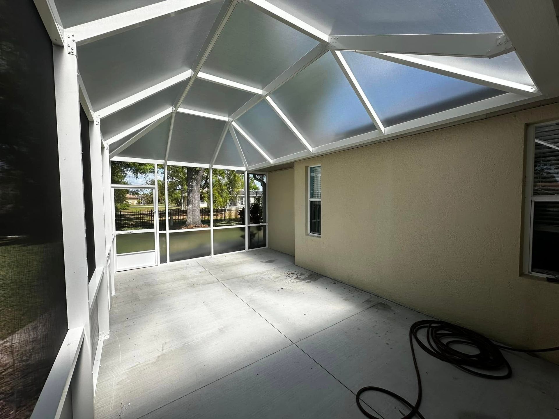 Covered patio with screened ceiling, concrete floor, beige wall, and sliding glass doors opening to a yard