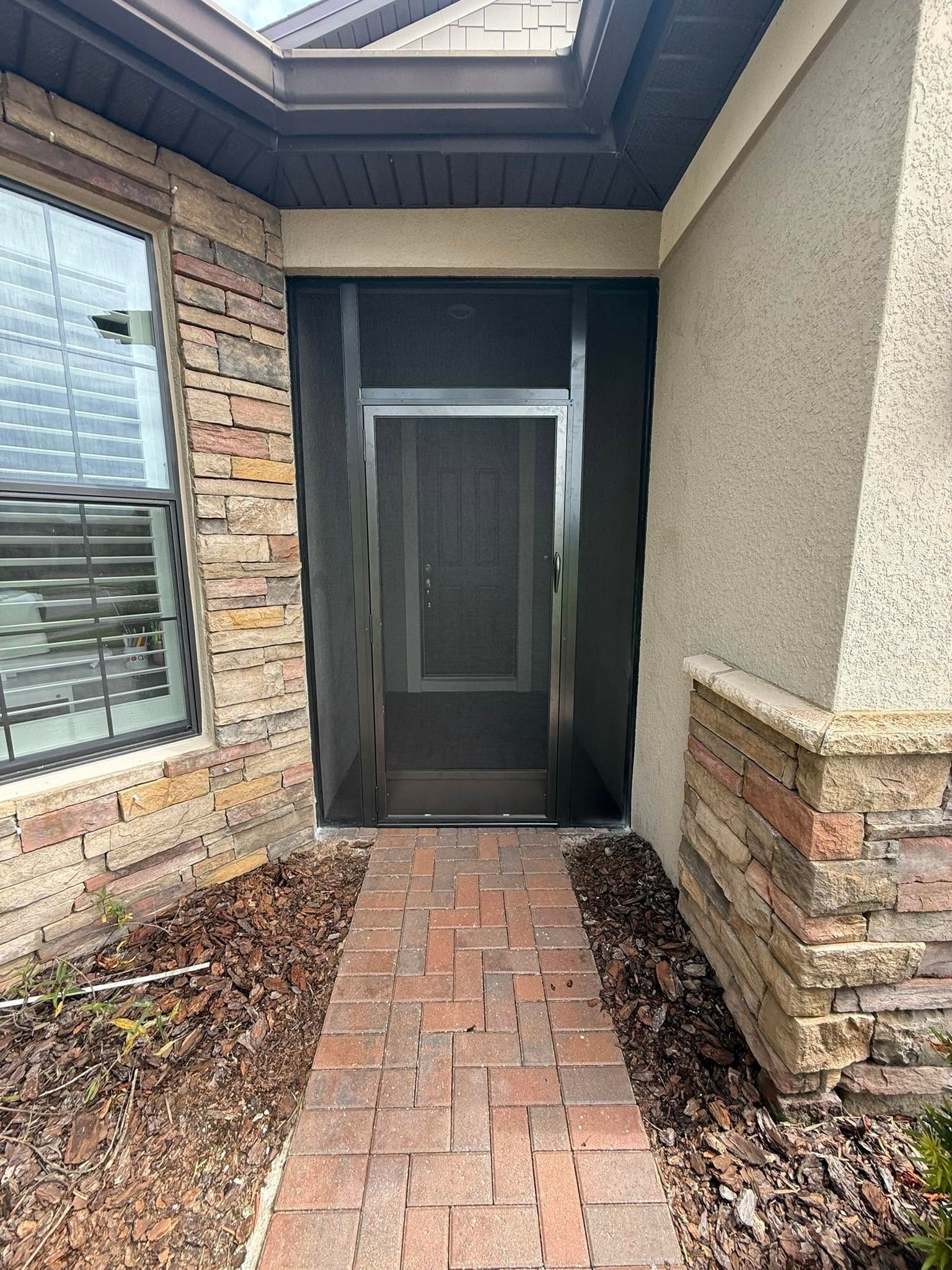 Front entry with dark screen door, brick walkway, and stone-accented porch under a covered roof.