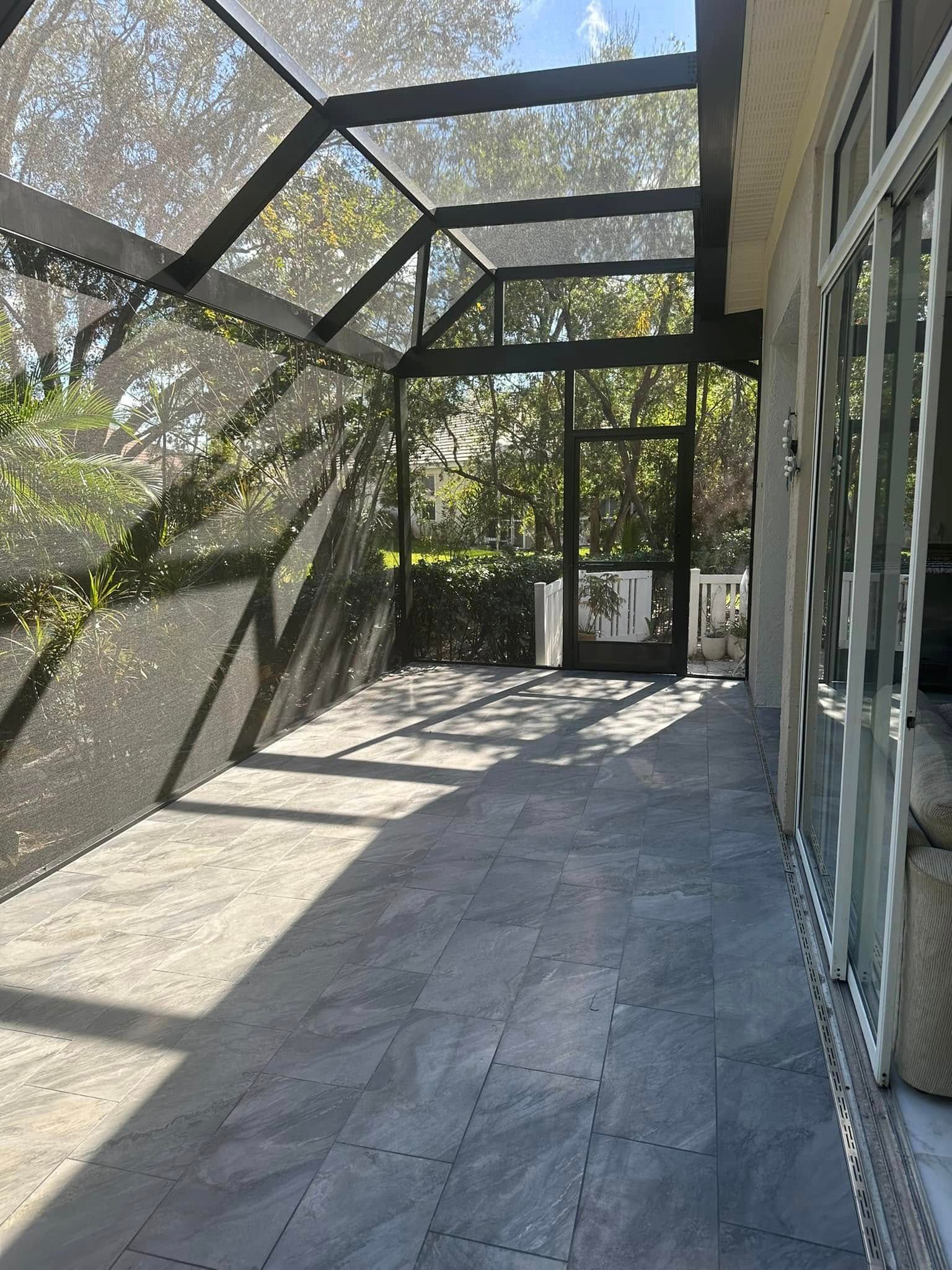 Screened patio corridor with metal-framed roof and glass doors, sunlight casting shadows on concrete floor