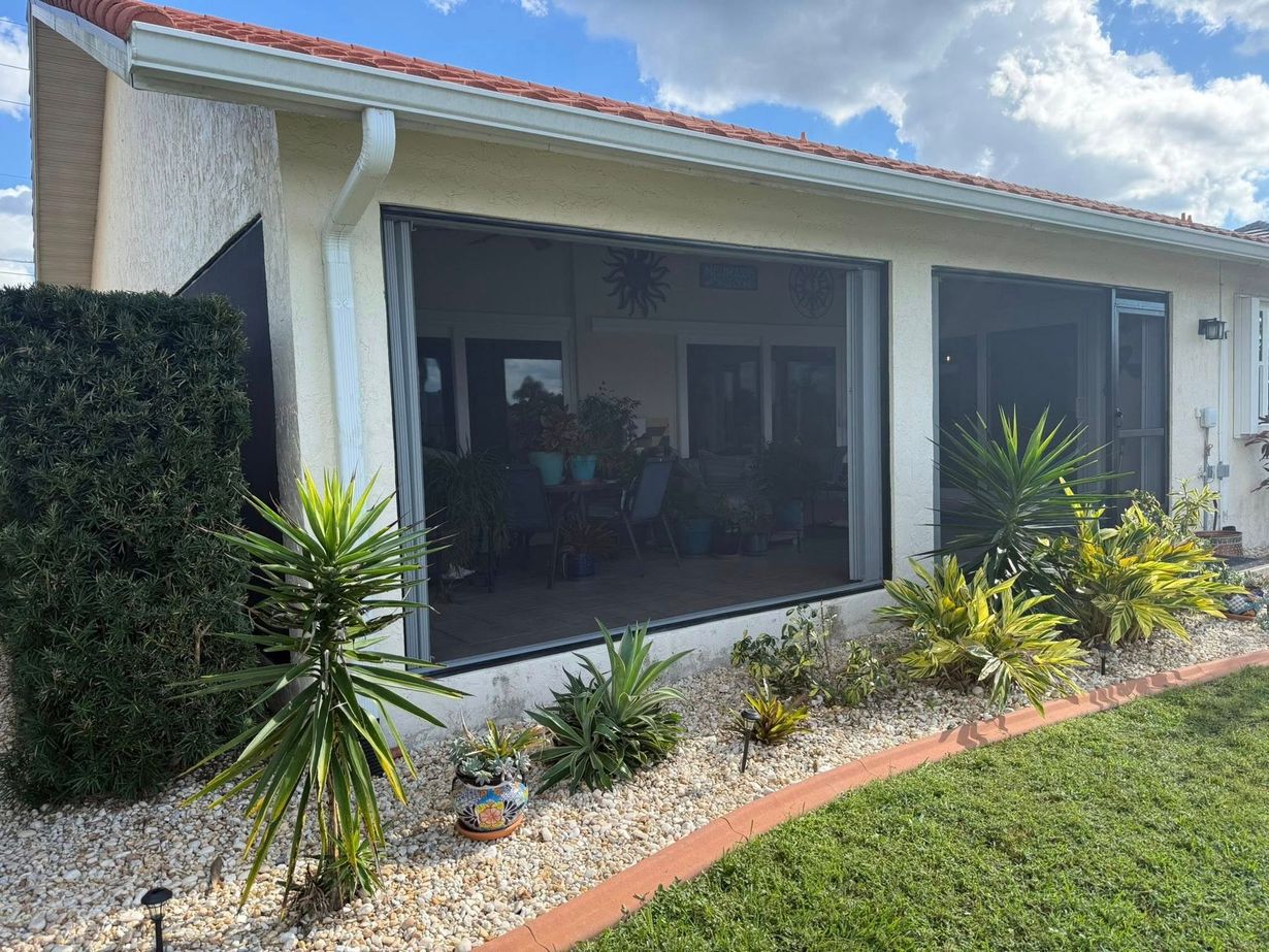 Single-story home with large screened porch, tropical plants, and a green lawn.