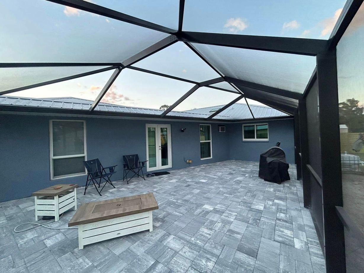 Back patio with gray pavers, dark screened enclosure, patio seating, and grill under a geometric roof frame