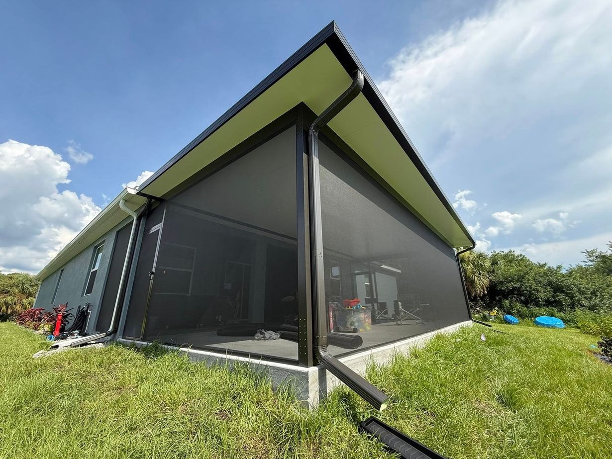 Modern house with dark screened walls and a sloped roof on a grassy hillside under a blue sky