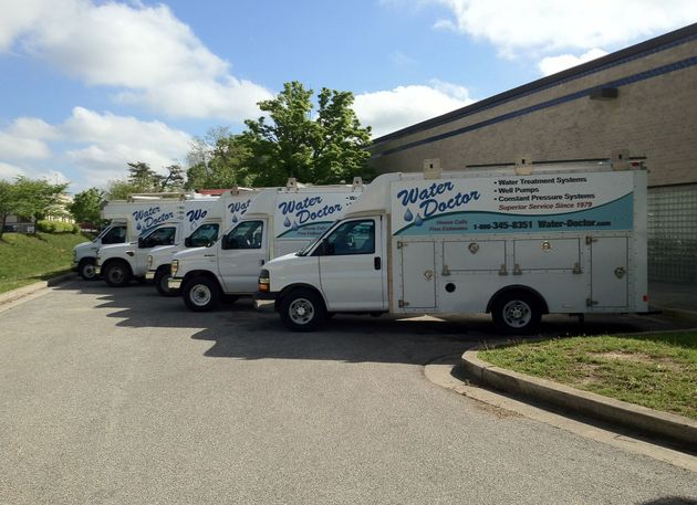 White service trucks with blue lettering parked beside a building on a sunny day.