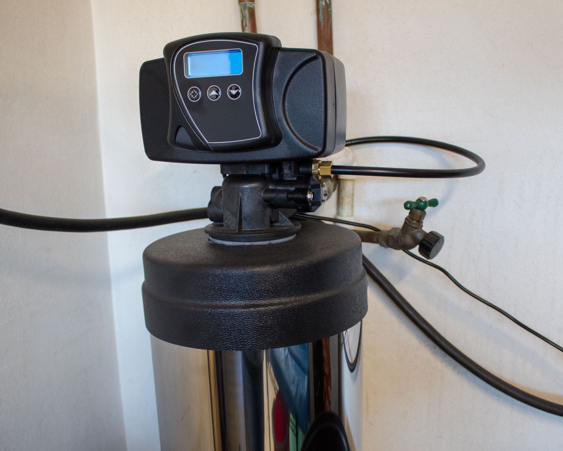 Water softener control head with digital display and hoses against a wall