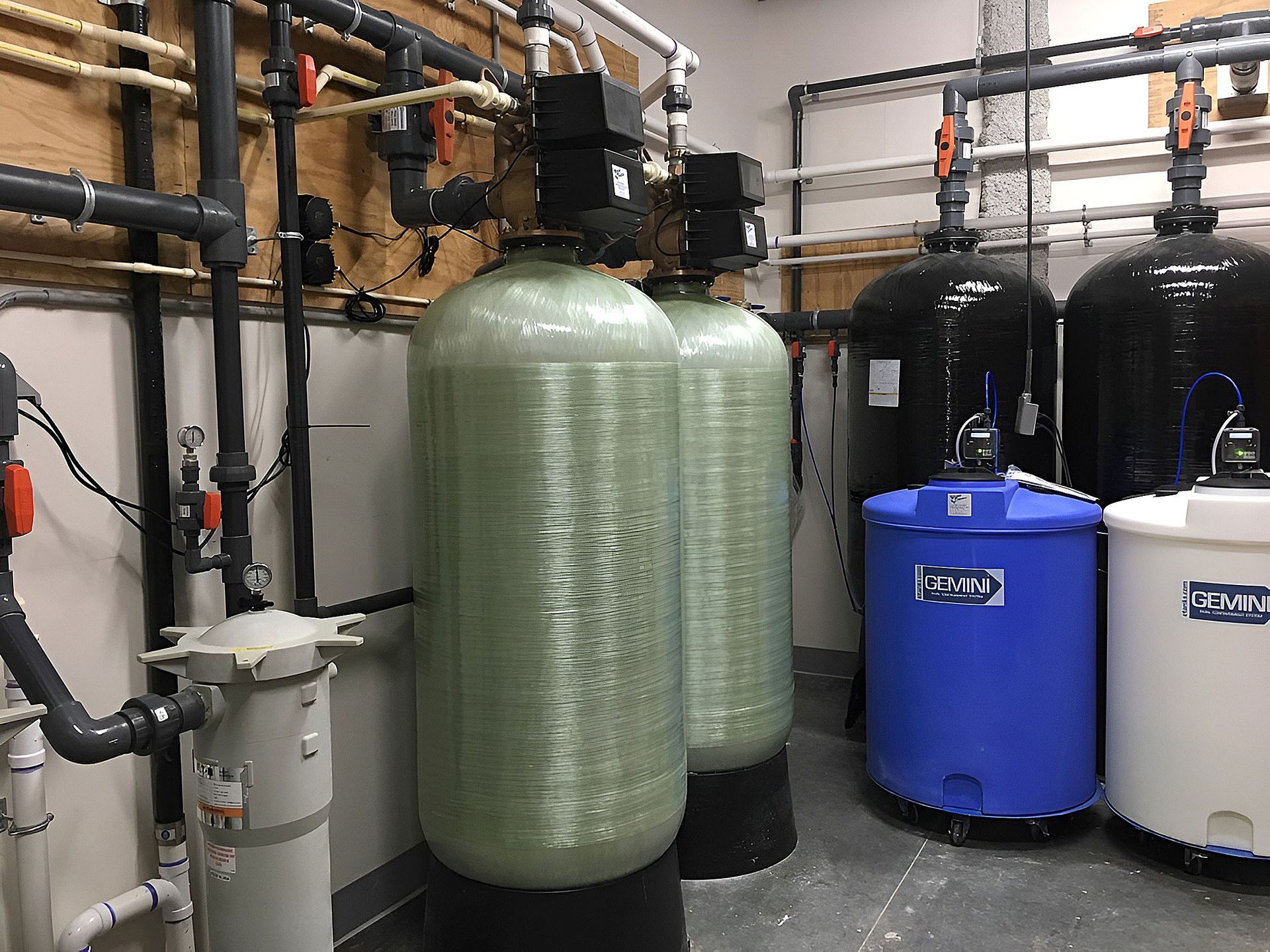Industrial water treatment room with blue tanks, silver cylinders, and exposed pipes