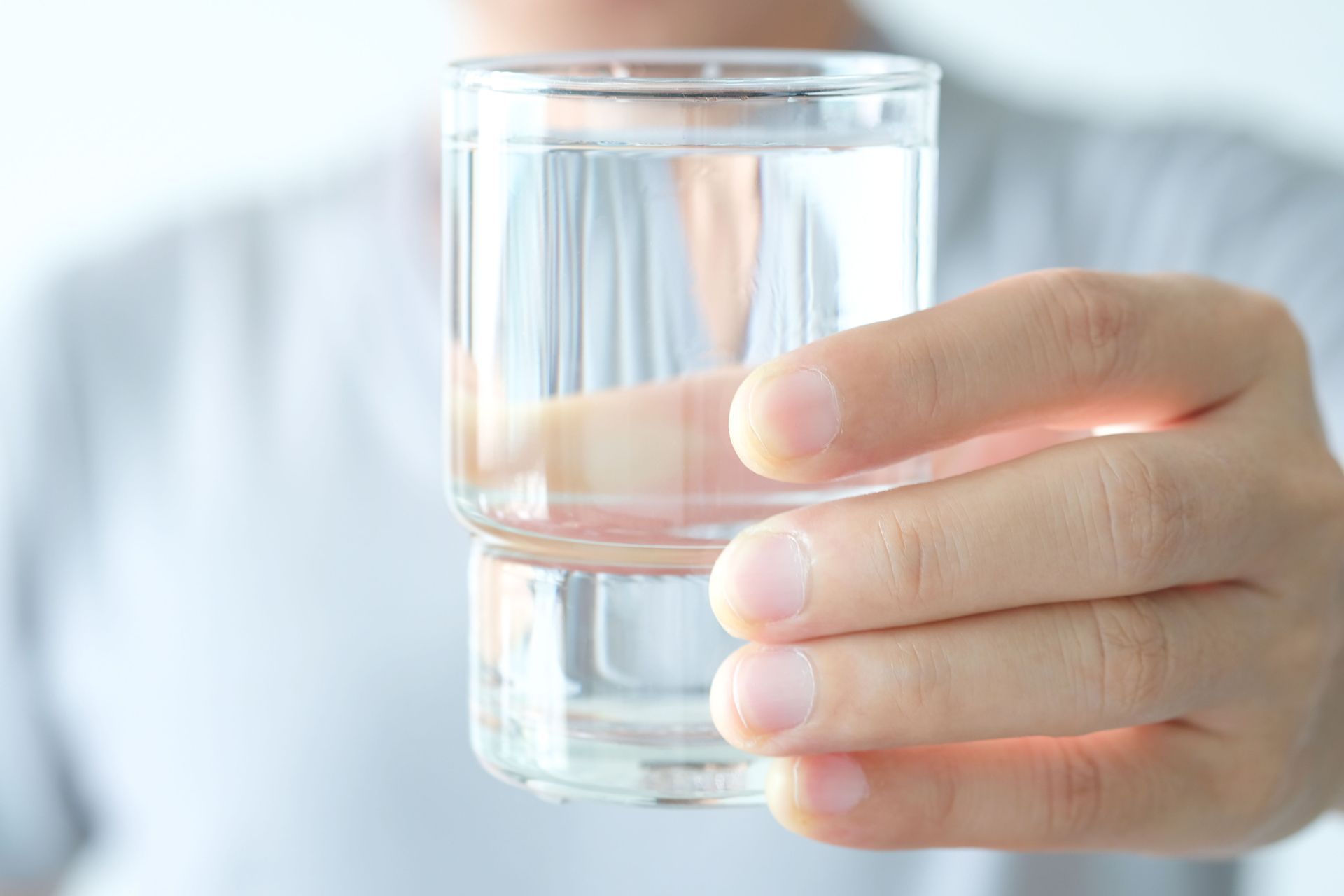 Hand holding a clear glass of water against a light background