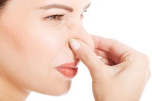 Woman pinching her nose with a hand, showing discomfort against a white background