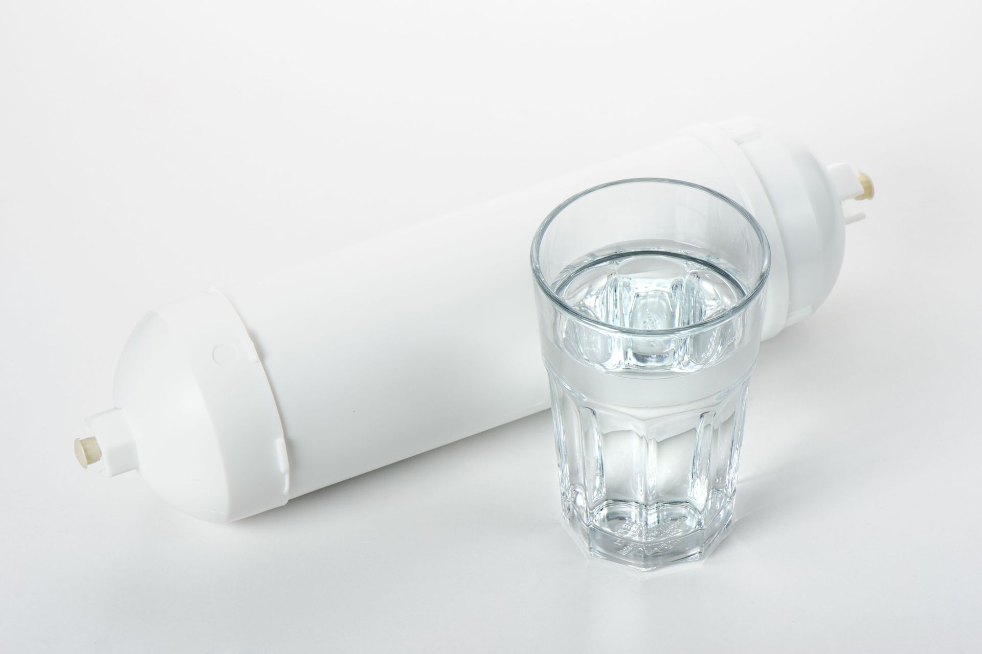 Clear glass of water beside a white rolled towel or cylinder on a white background