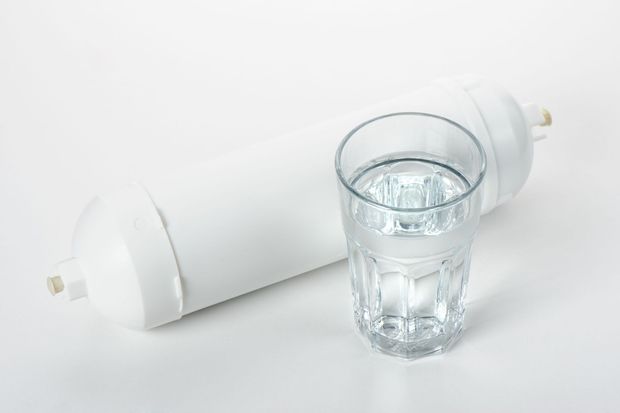 Clear glass of water beside a white rolled towel or cylinder on a white background