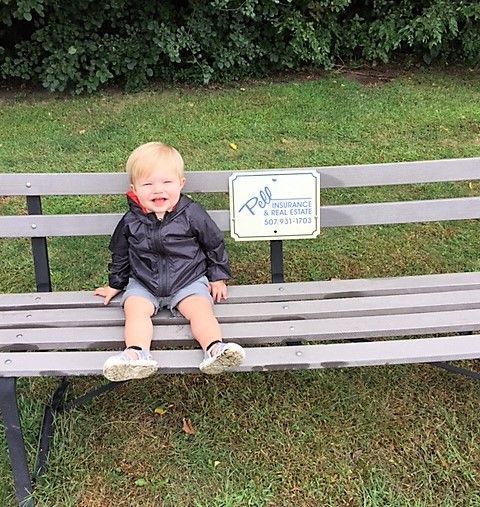 A baby sitting on a bench with Pell Insurance and Real Estate signage
