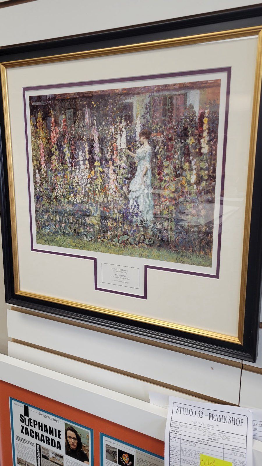 A framed painting of a woman in a white dress standing in a garden.