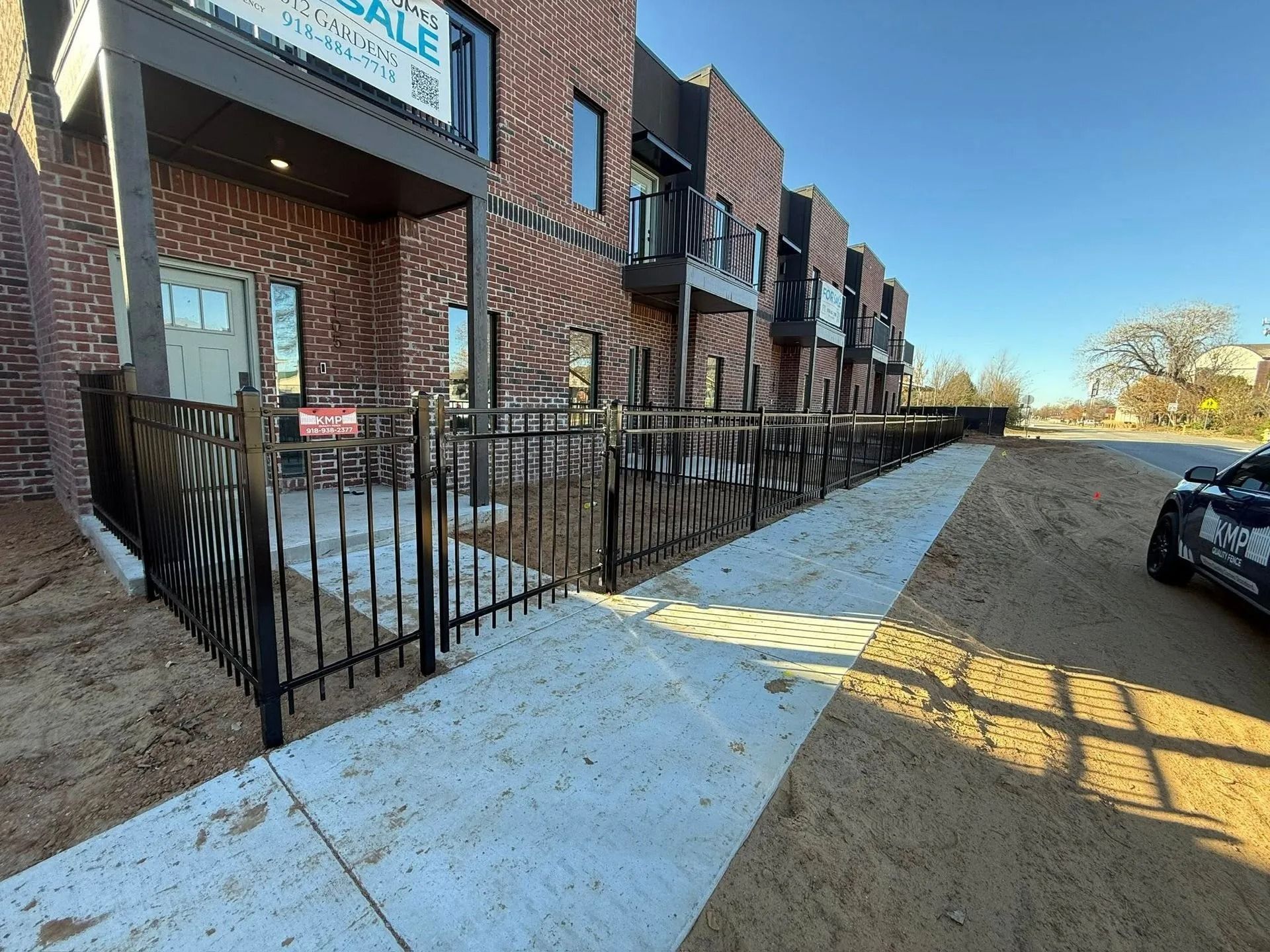 Row of brick townhouses with black metal fences and a concrete sidewalk.