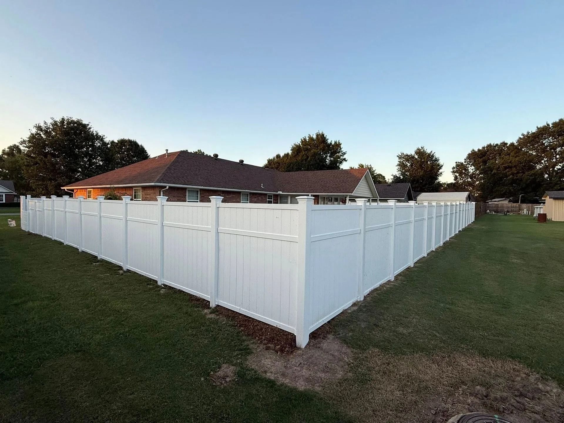 White vinyl fence surrounding a grassy yard, house in the background.