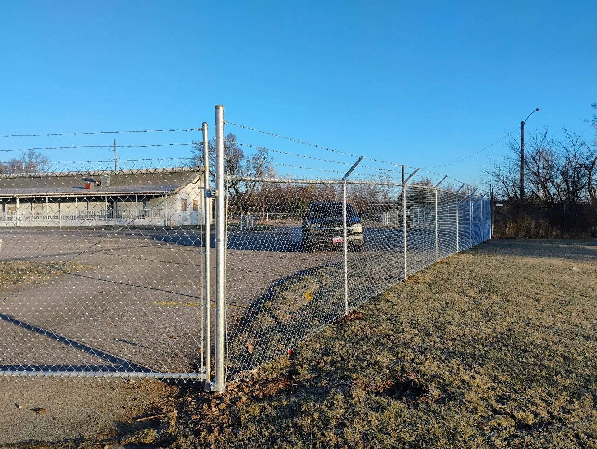 Chain-link fence with barbed wire on a sunny day; a building visible beyond the fence.