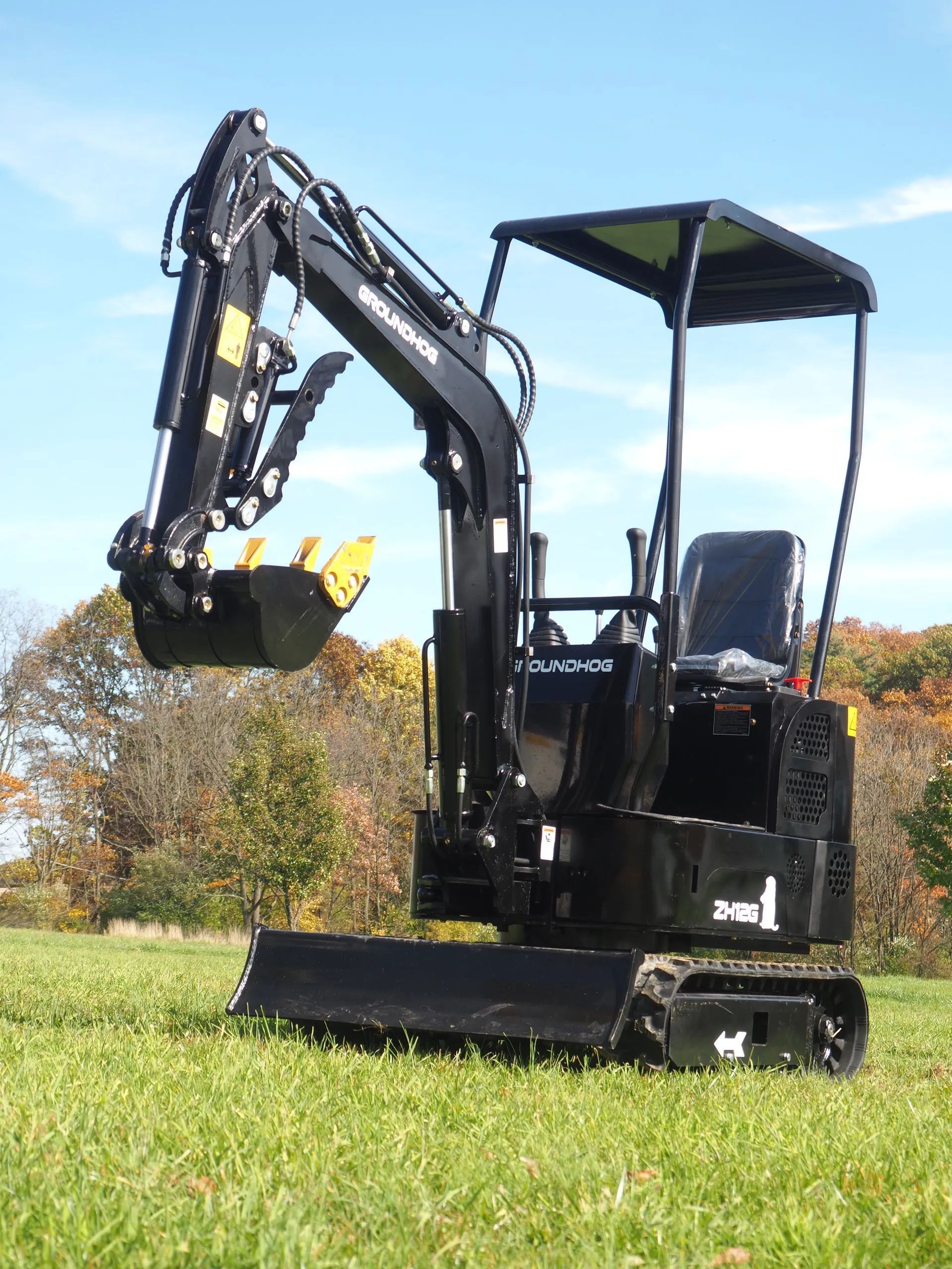 A black mini excavator parked on a grassy field under a clear blue sky.
