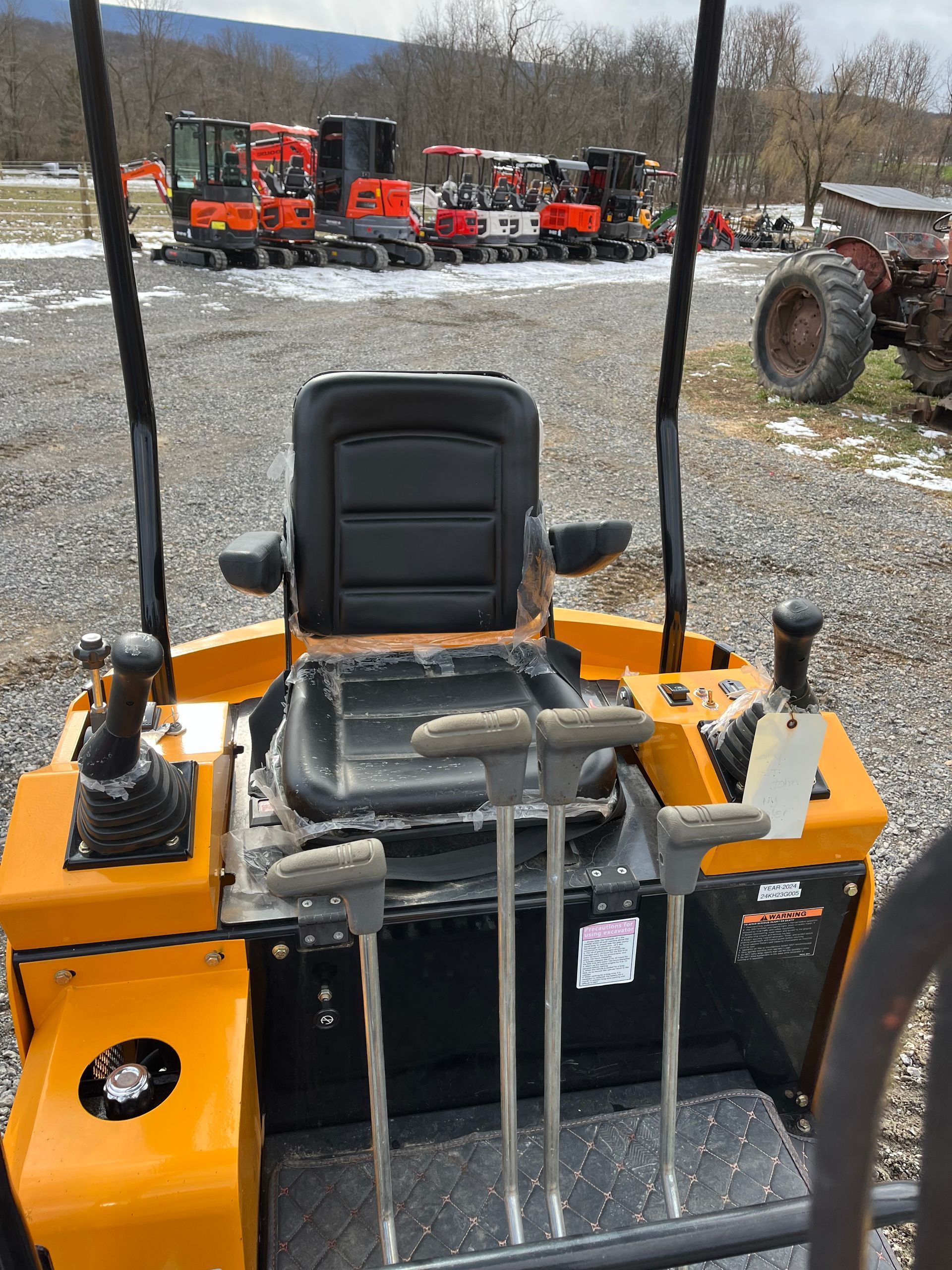 A driver's view from a yellow construction vehicle showing the seat, controls, and levers, with more machines in the yard.