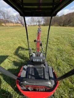 View from the operator's seat of a red compact excavator in a grassy field.