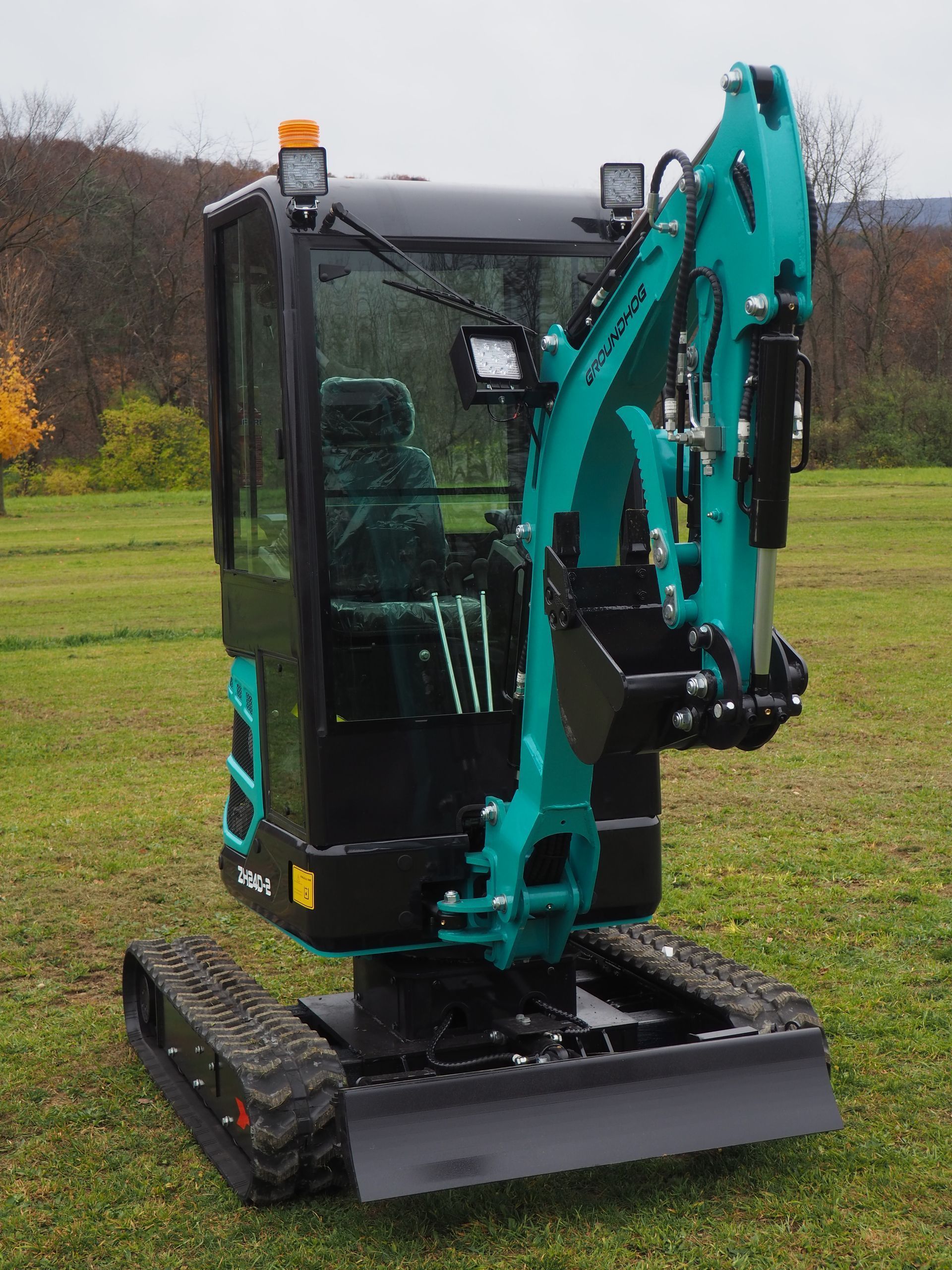 Teal mini excavator with a closed operator cab parked on a grassy field.