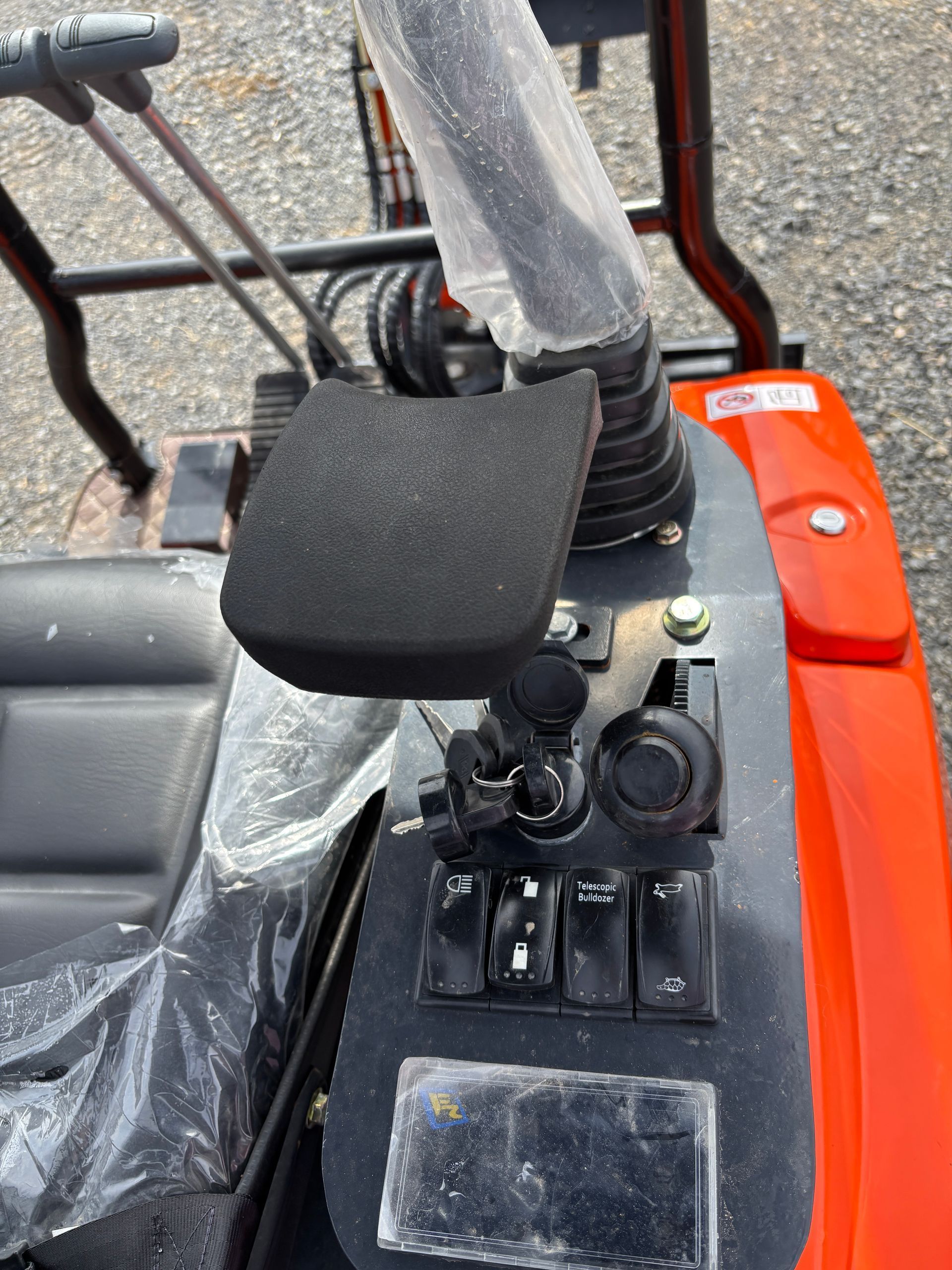 Controls of an orange piece of machinery with joysticks, switches, and a key ignition on a black panel.