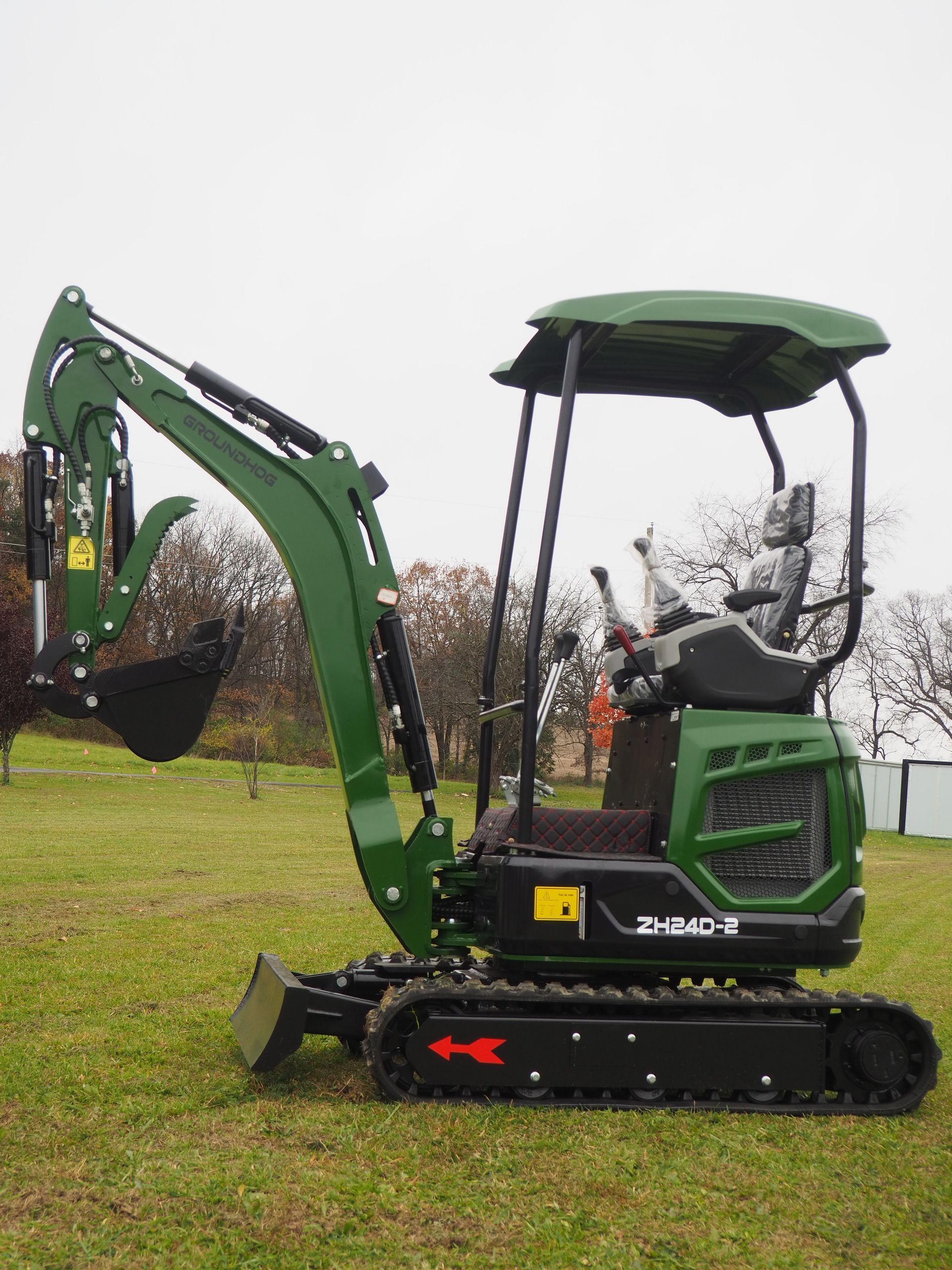 A green, compact excavator sits on a grassy field with a canopy and black crawler tracks.