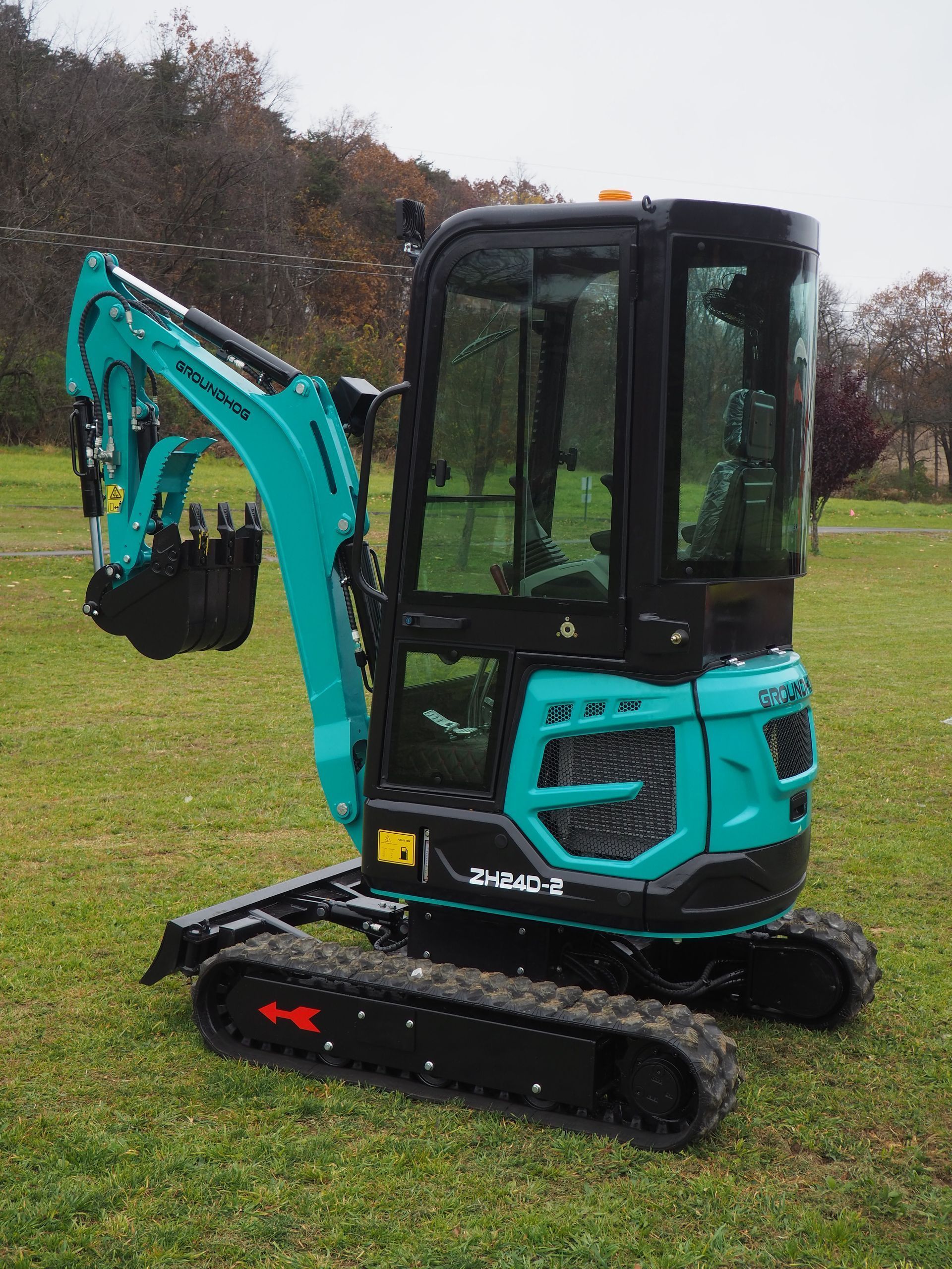 A turquoise mini excavator parked on grass, angled to the side with its cabin and front bucket visible.
