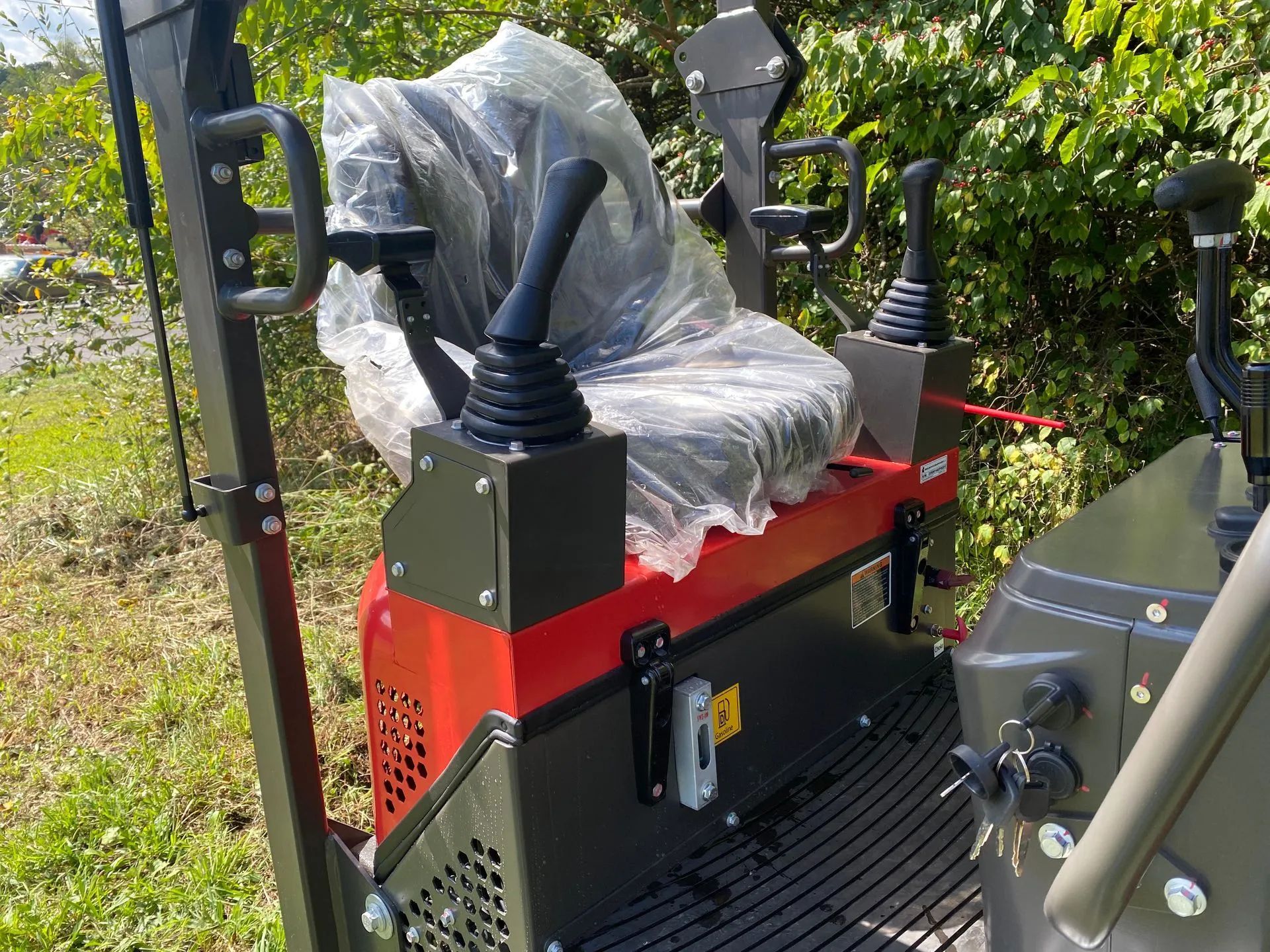 The operator's seat and control joysticks of a red and black industrial piece of equipment outdoors.