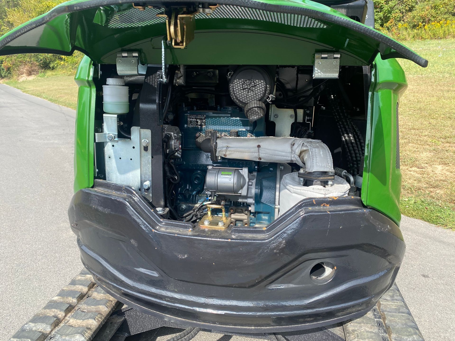 Rear view of a green mini excavator with its engine compartment cover open, revealing the engine components.