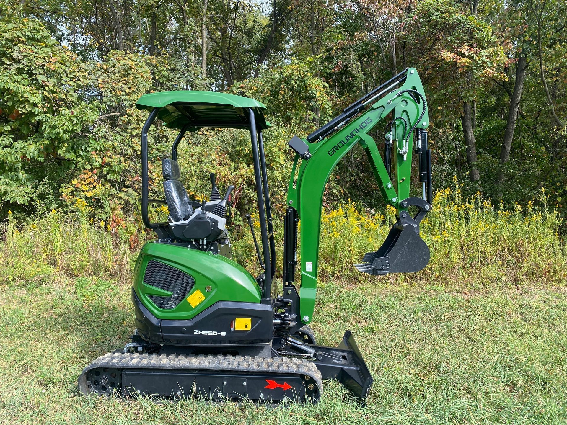 A bright green mini excavator sits on a grassy field in front of a line of trees.