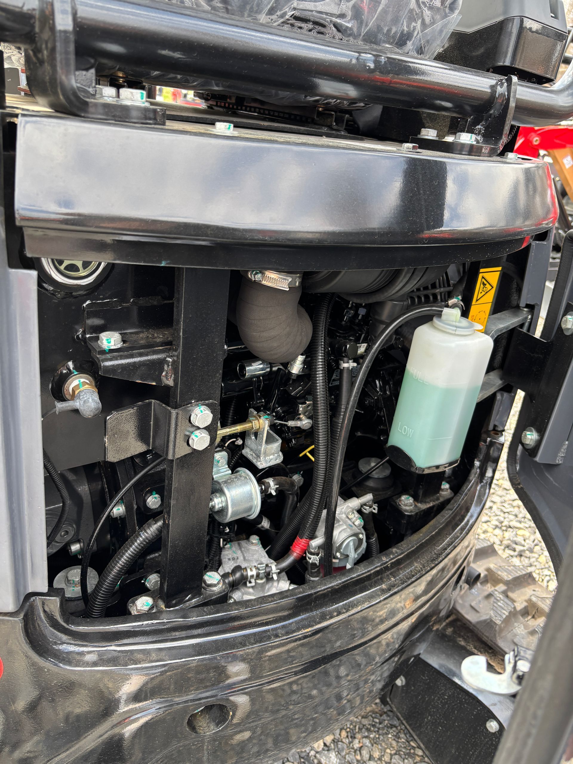 Engine compartment of a small excavator featuring a coolant reservoir and various mechanical components.