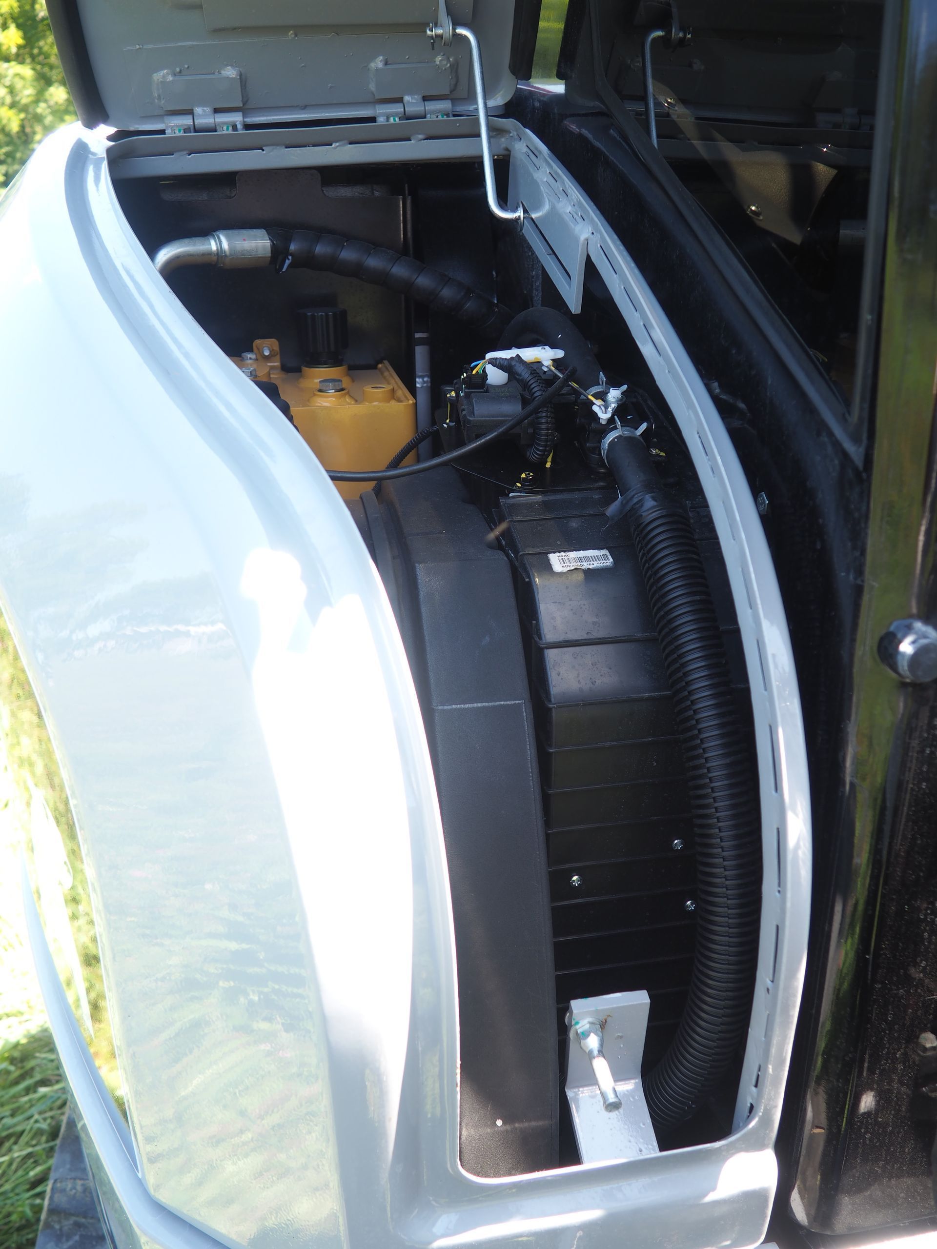Open compartment of a piece of heavy machinery, showing a black radiator, yellow hydraulic component, and black hoses.