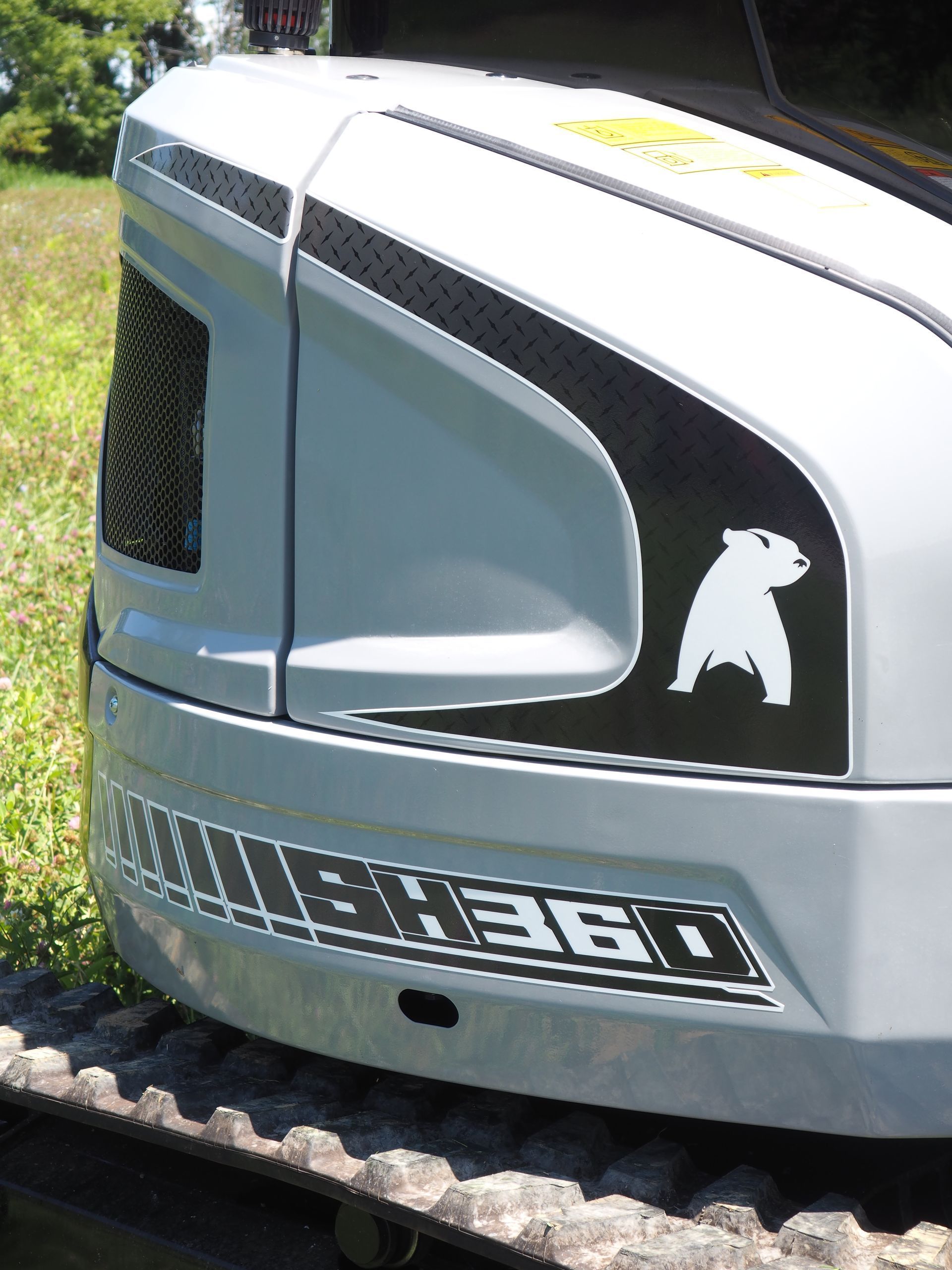 A close-up of a grey excavator featuring a black decal with a white bear silhouette and 