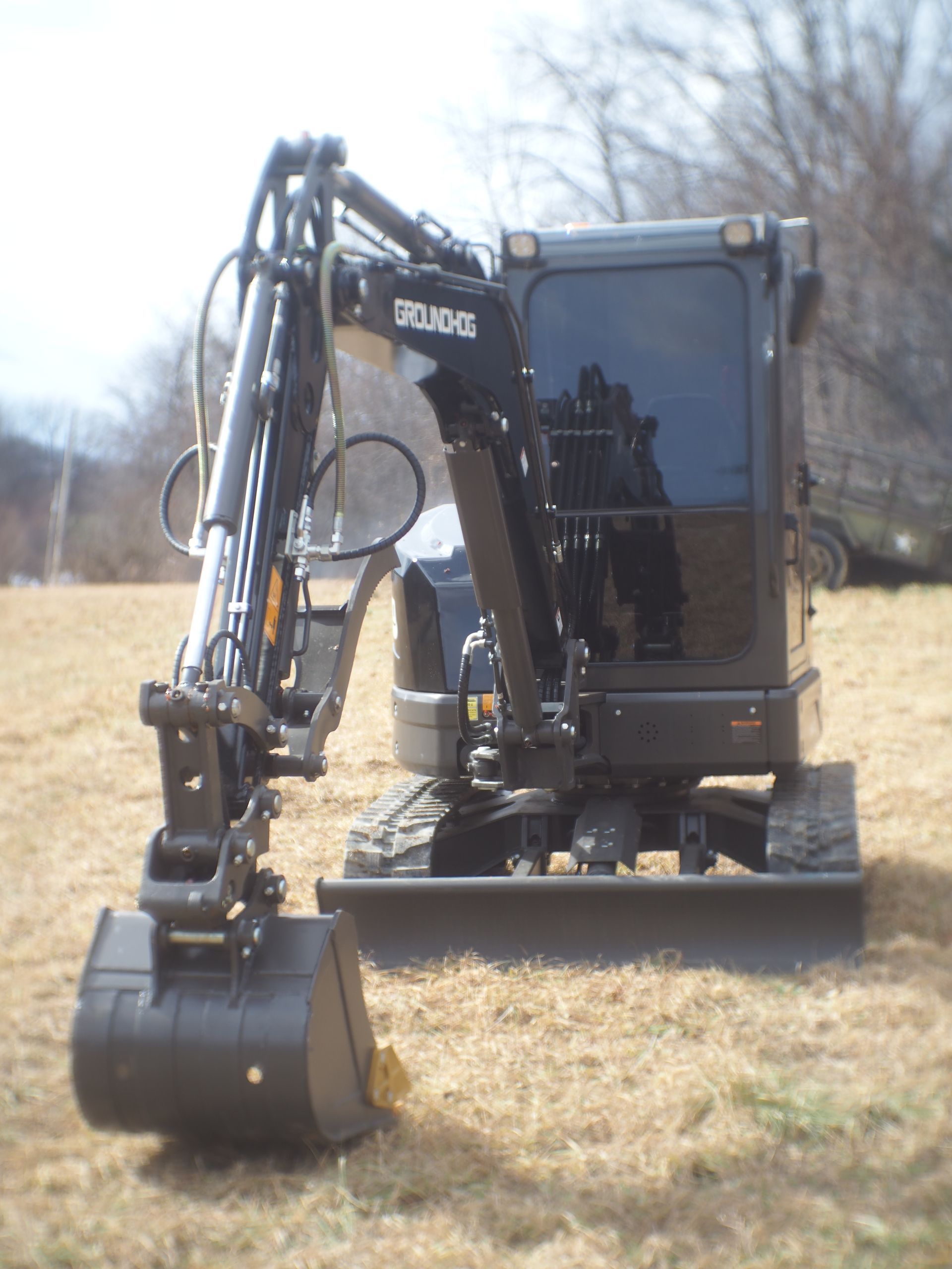 A black mini-excavator sits on dry grass in an open field under a bright sky.