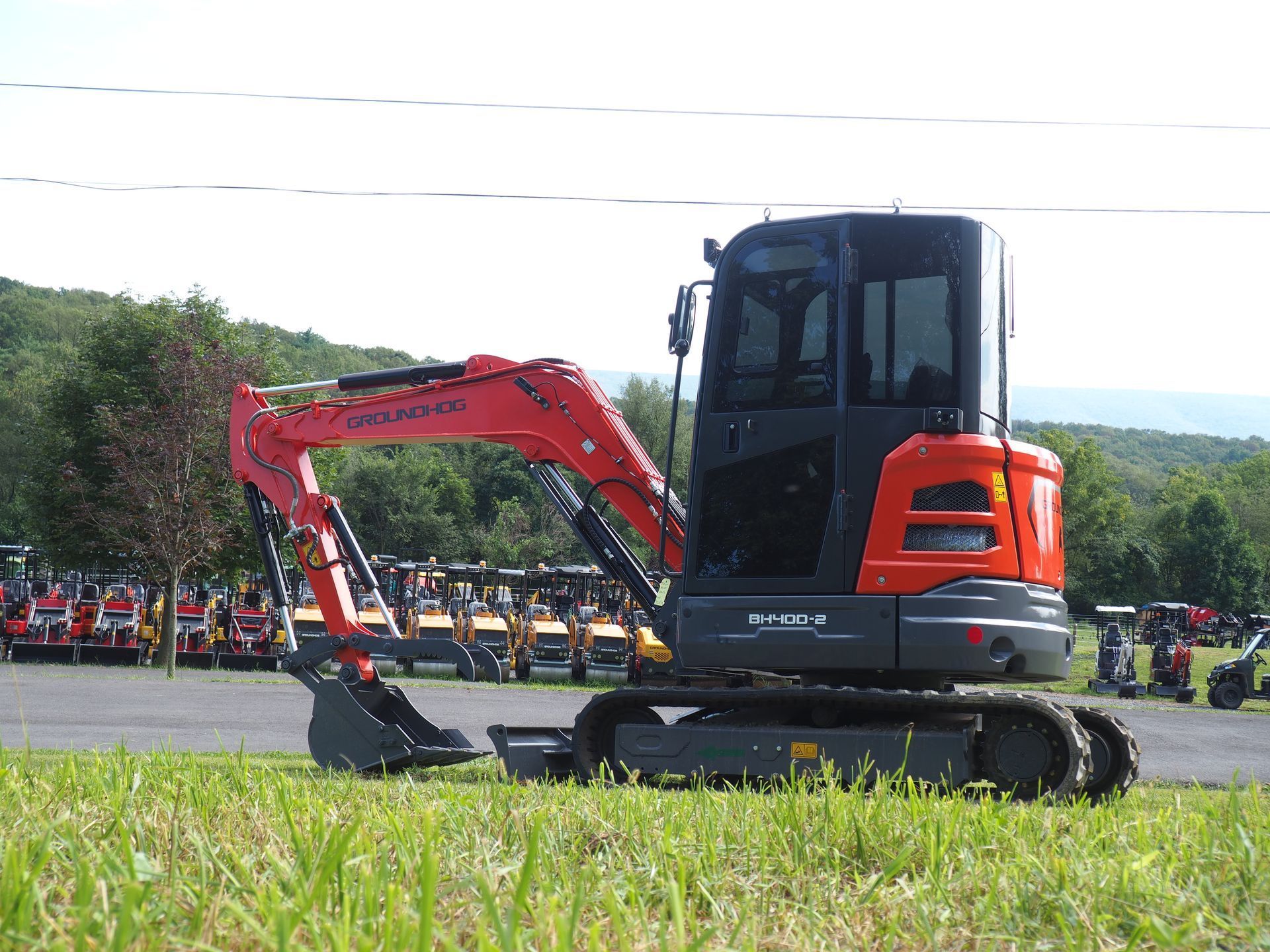 A bright orange Kubota mini excavator parked on a grassy field in front of a lot filled with other construction equipment.