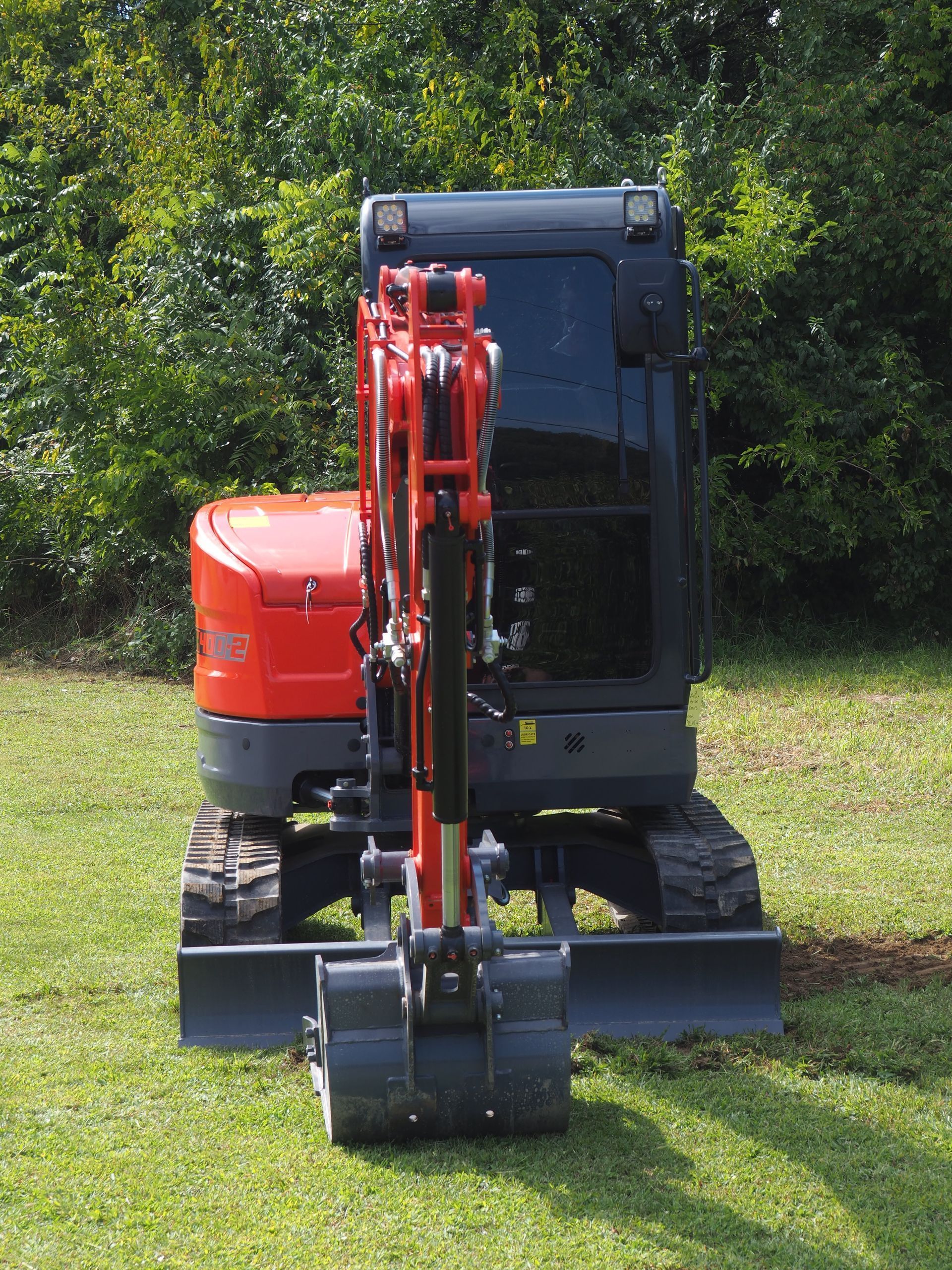 An orange Kubota compact excavator parked on a grassy field, viewed from behind.