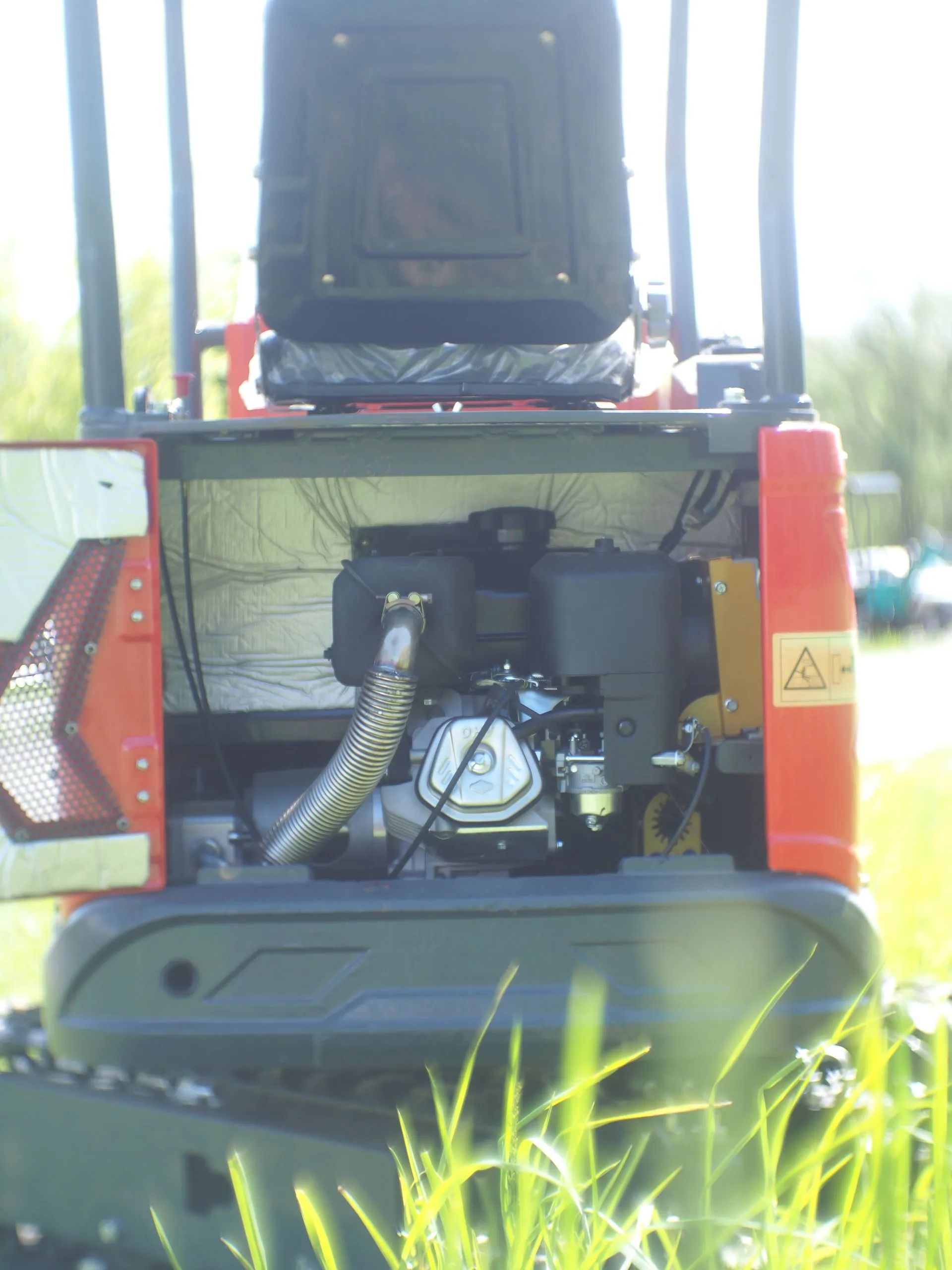 Rear view of an orange mini excavator with its back engine compartment cover open, revealing the engine components.