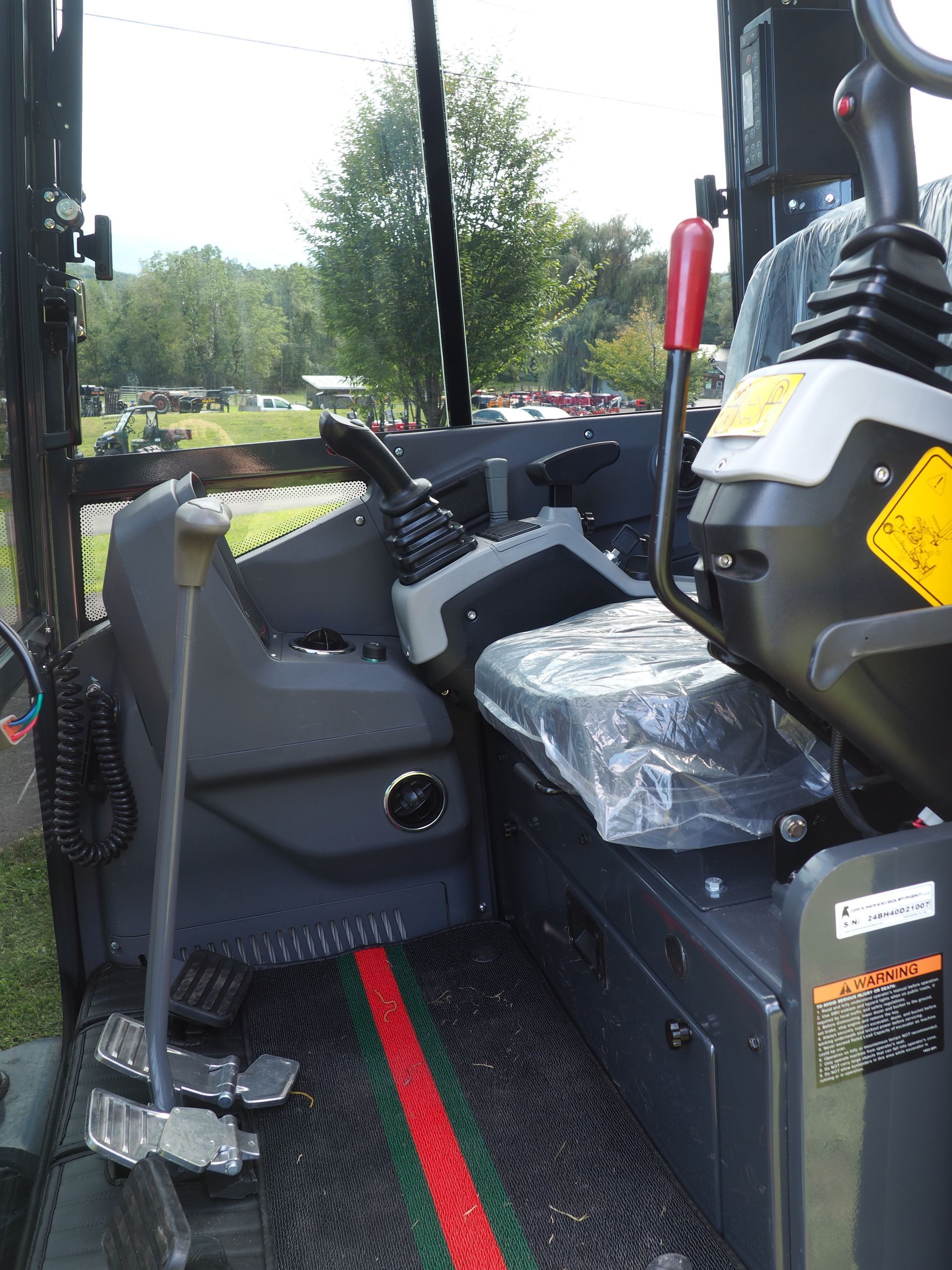 Interior view of an excavator cab showing the operator's seat, joysticks, controls, and foot pedals.