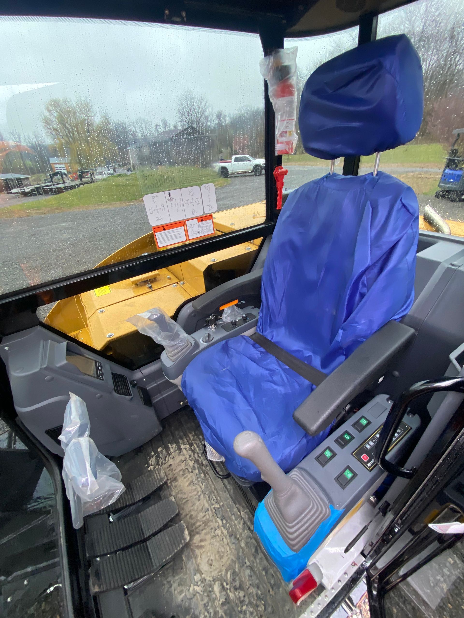 The interior of a construction vehicle cabin featuring a bright blue seat cover and control joysticks.