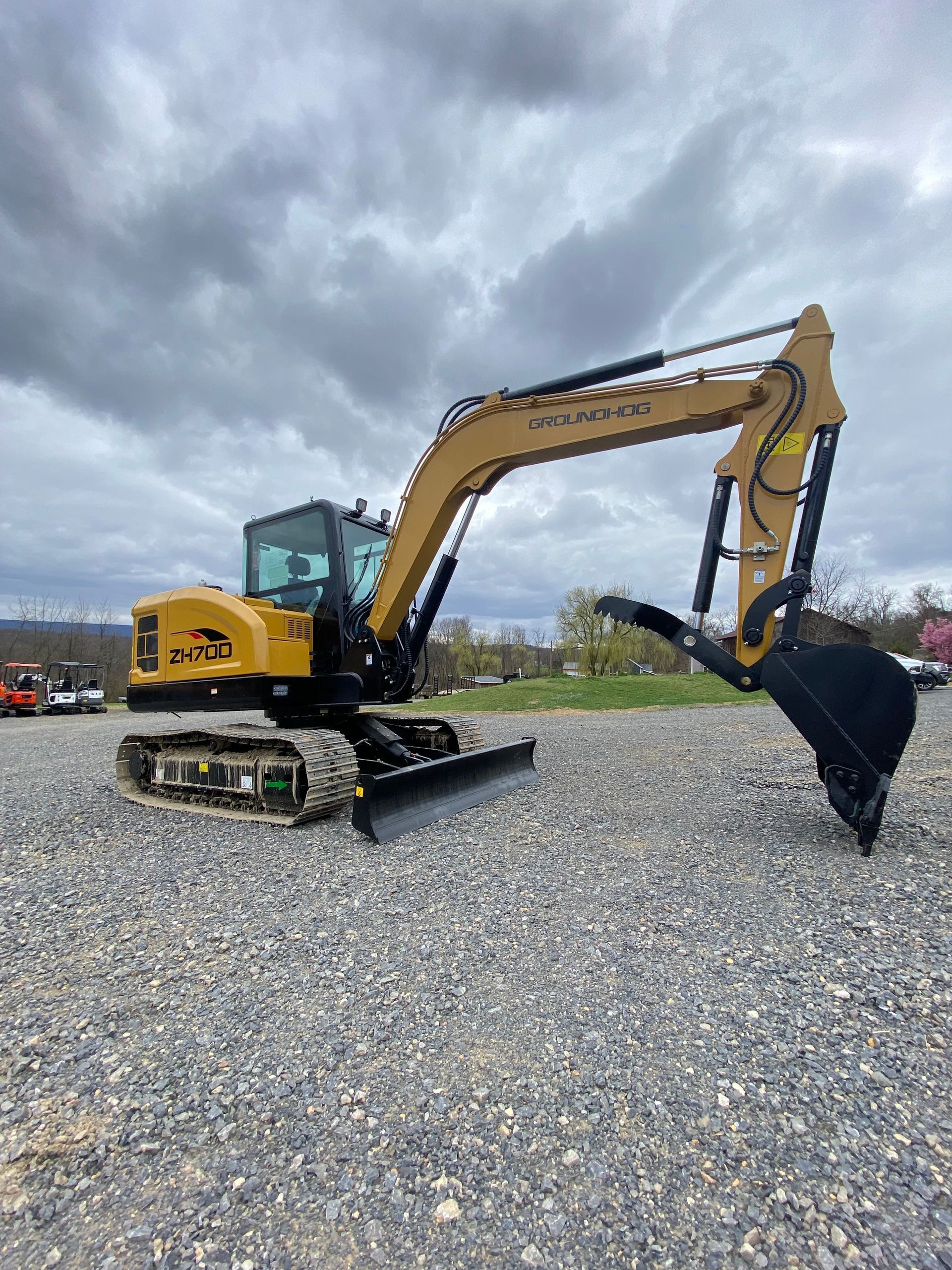 A yellow Caterpillar excavator with a bucket attachment parked on a gravel lot under a cloudy sky.