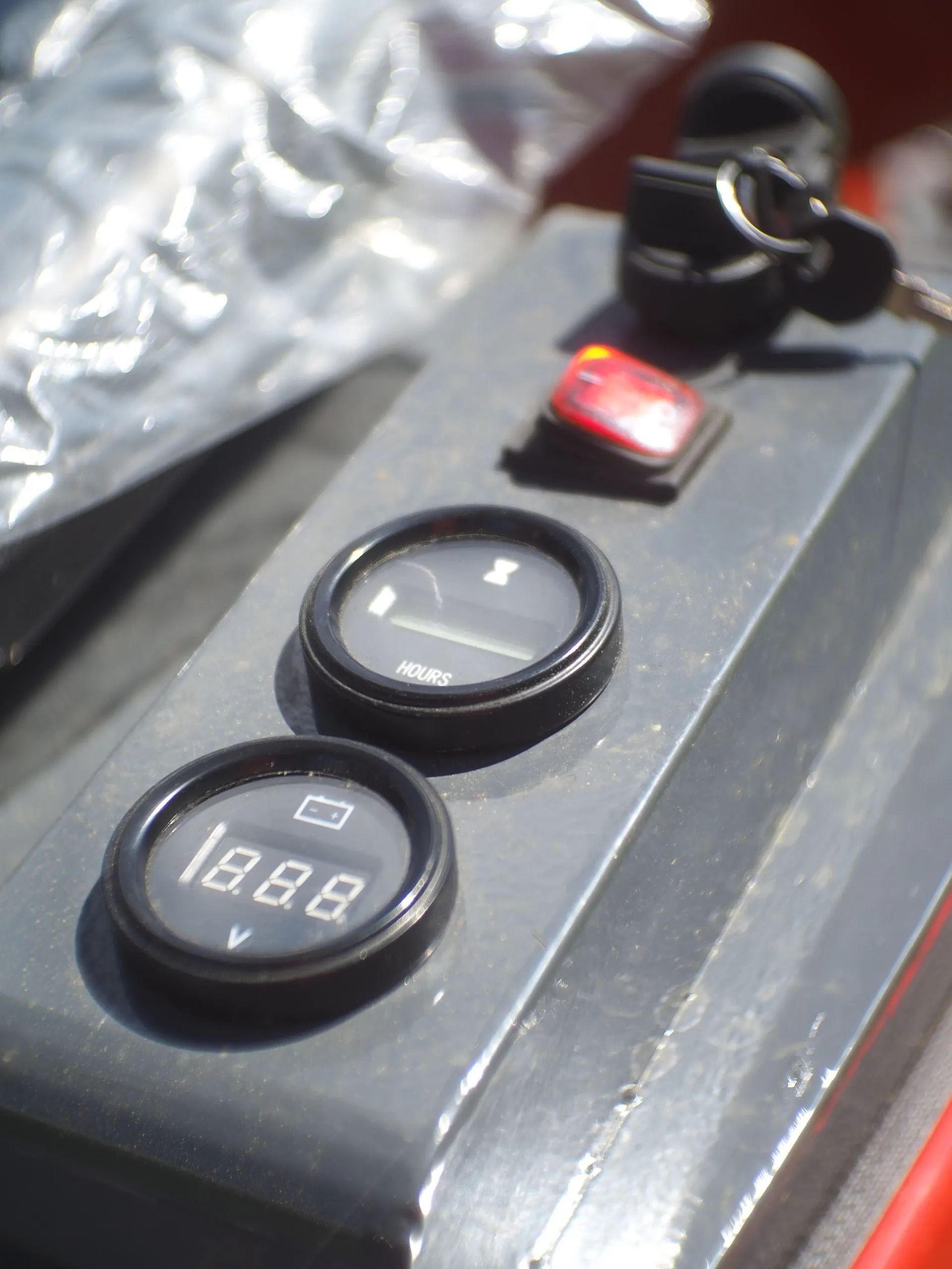 A gray control panel with a key ignition, a red toggle switch, an analog gauge, and a digital voltmeter display.