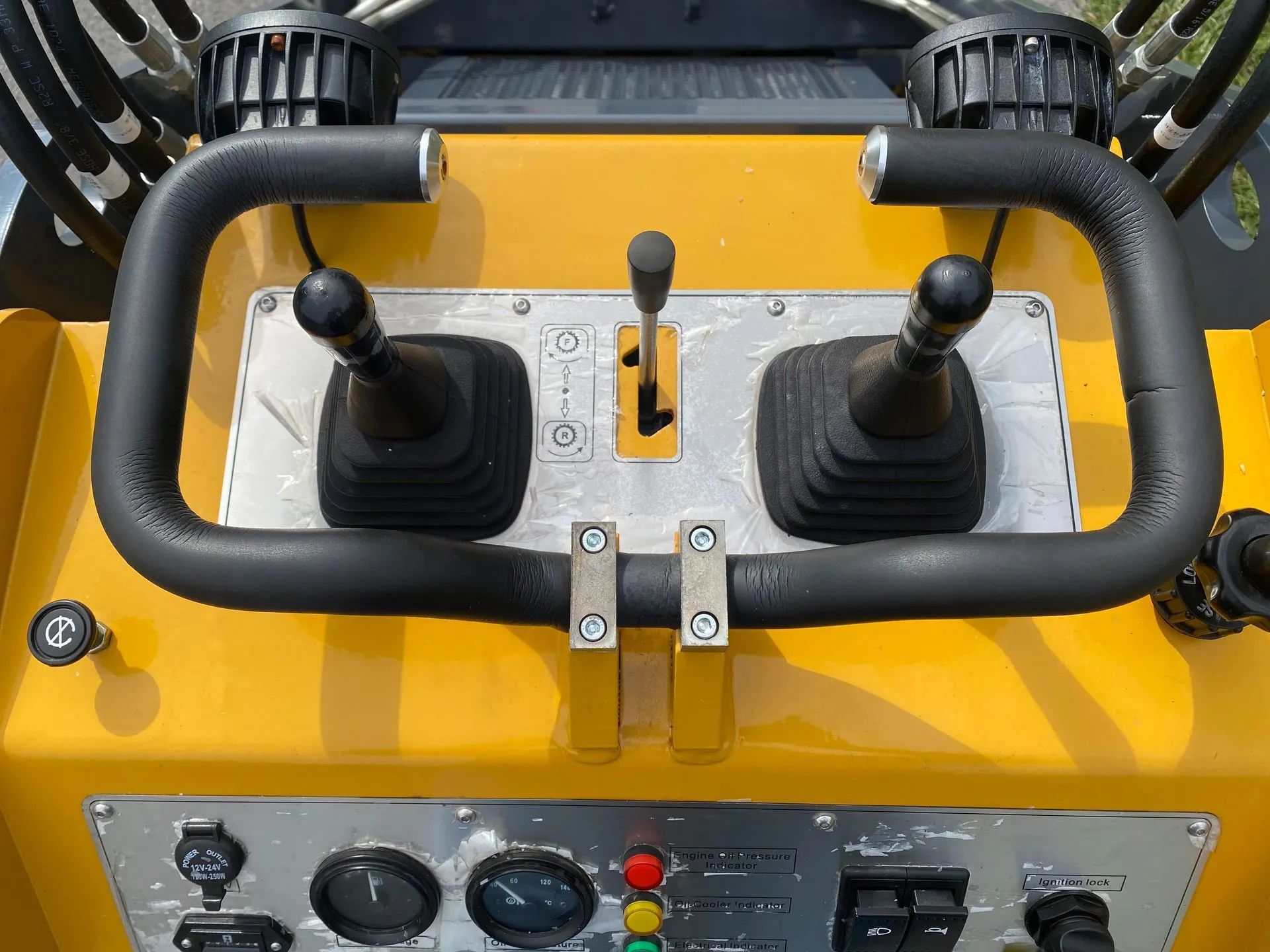 Bright yellow operator controls for heavy machinery, featuring two joysticks, a throttle lever, and various gauges.