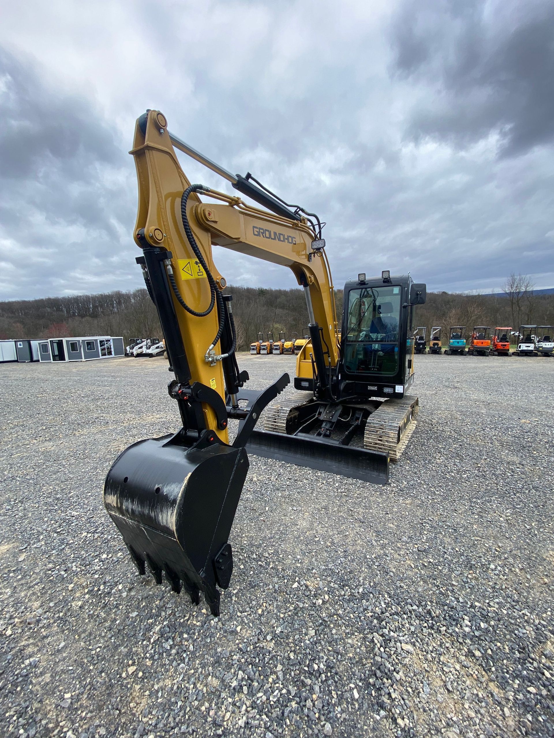 A yellow Caterpillar excavator with a black bucket parked on a gravel lot under a cloudy sky.
