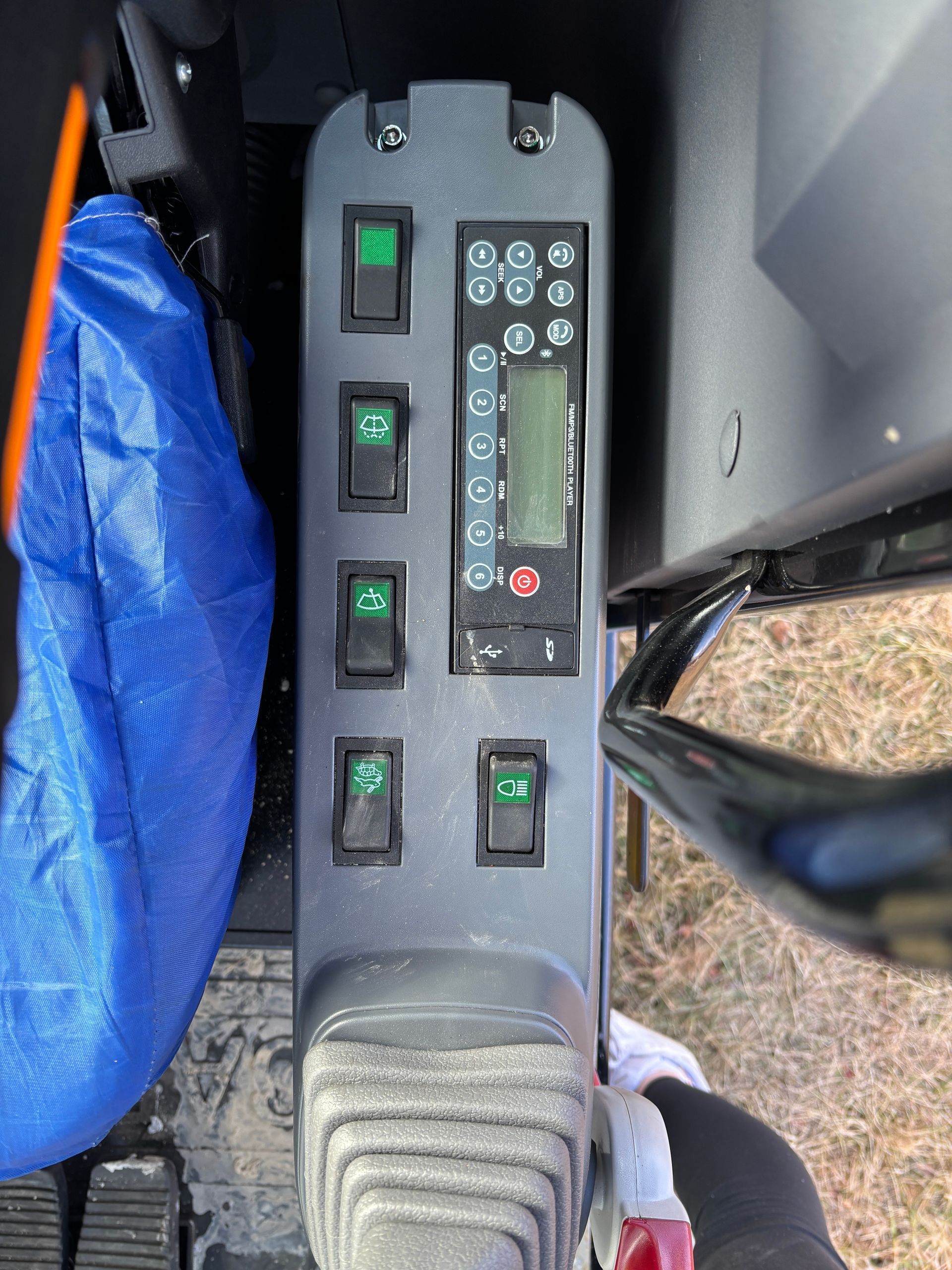 An interior console of heavy machinery featuring a digital display, buttons, and a joystick control.