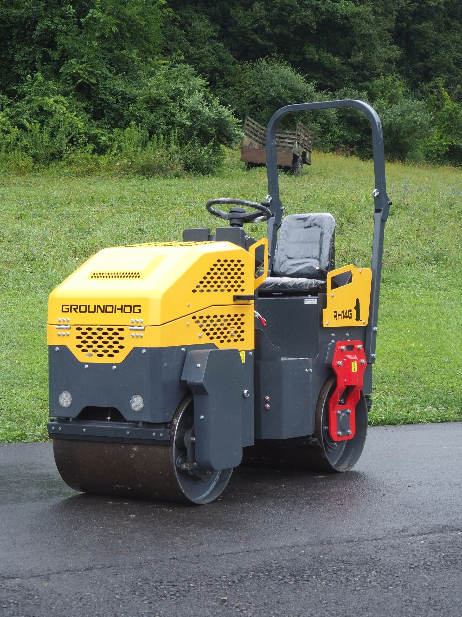 A small, yellow and dark gray Ground-hog asphalt roller sitting on a paved path in a grassy area.