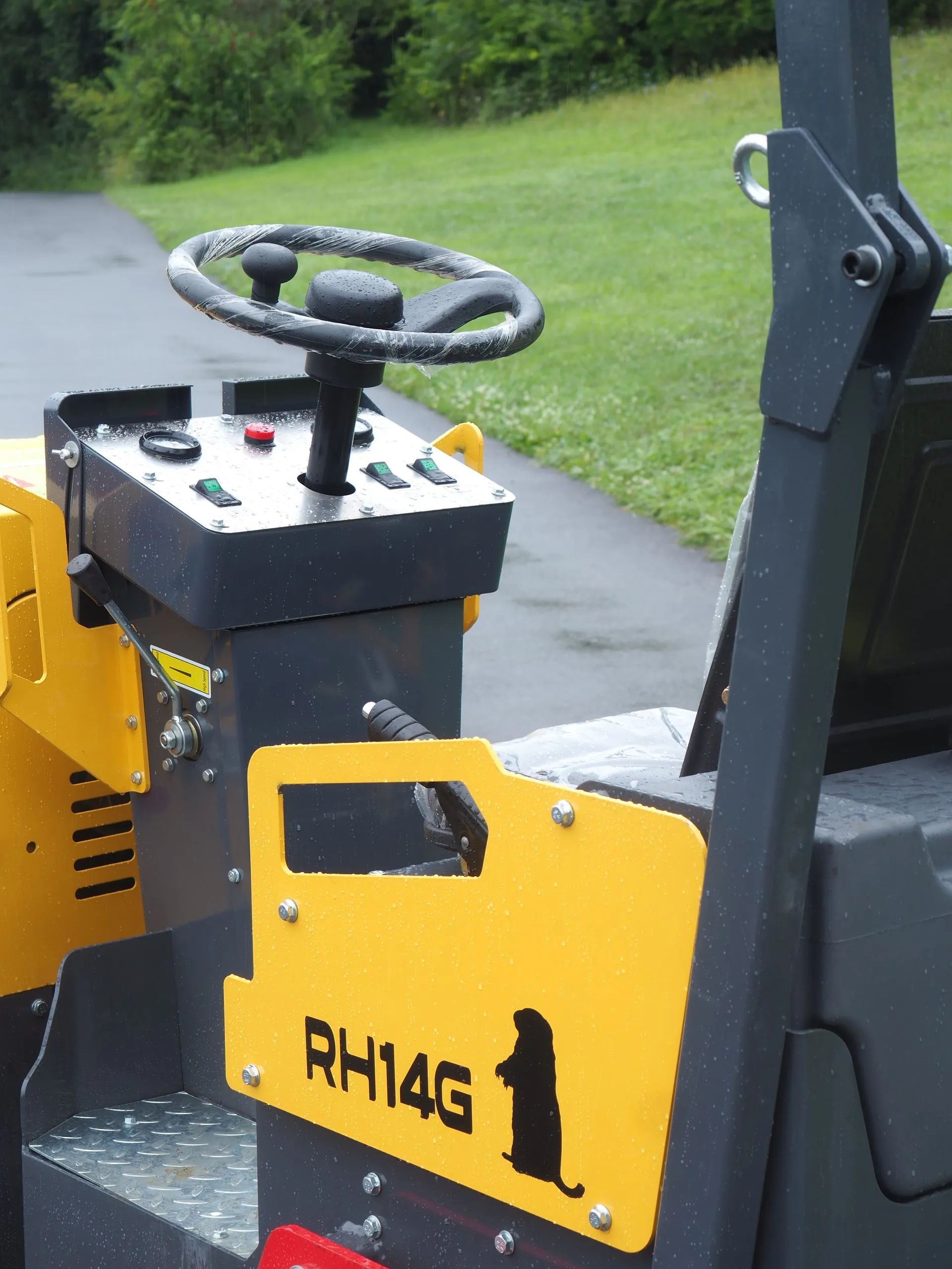 Yellow and gray industrial equipment labeled RH14G with a steering wheel and control panel, parked on a paved path.