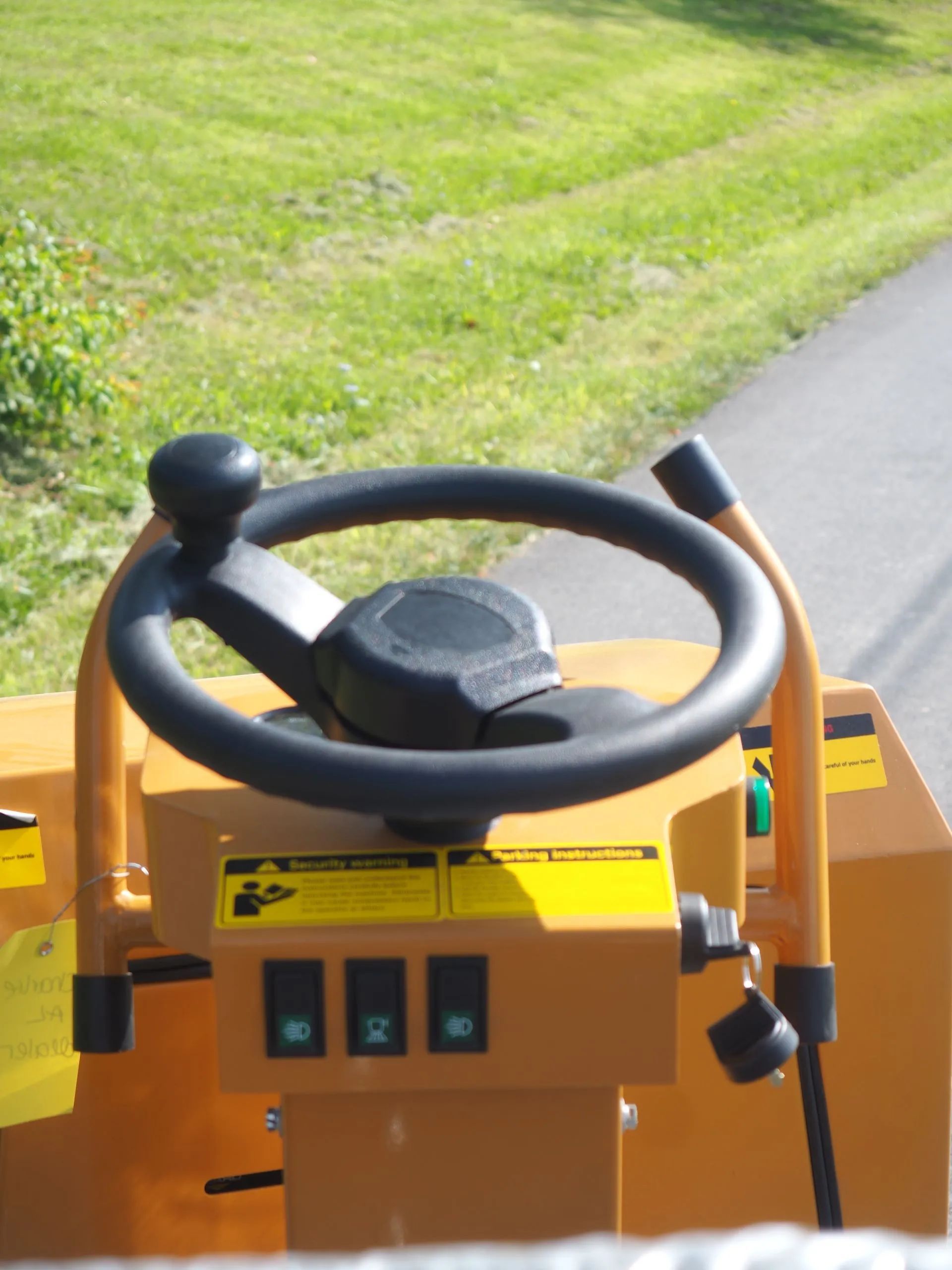 A close-up view of the black steering wheel and yellow control console of a construction vehicle.