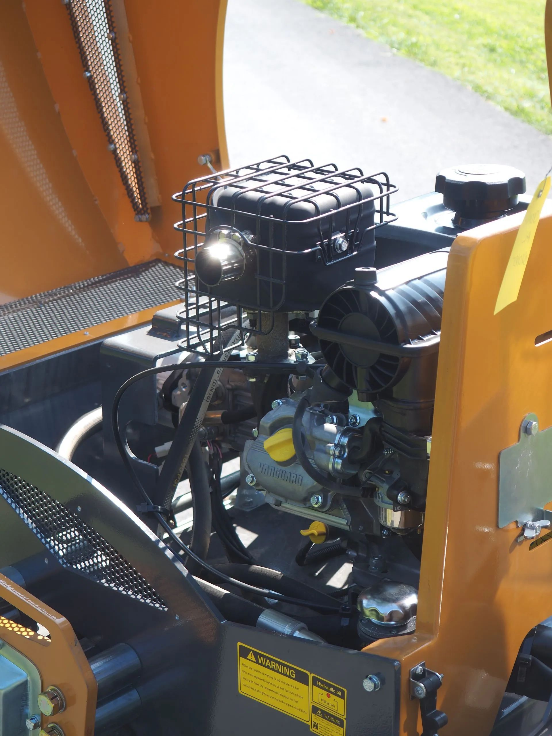 An open view of a yellow piece of machinery’s small engine, showcasing parts like the muffler guard, cap, and oil dipstick.