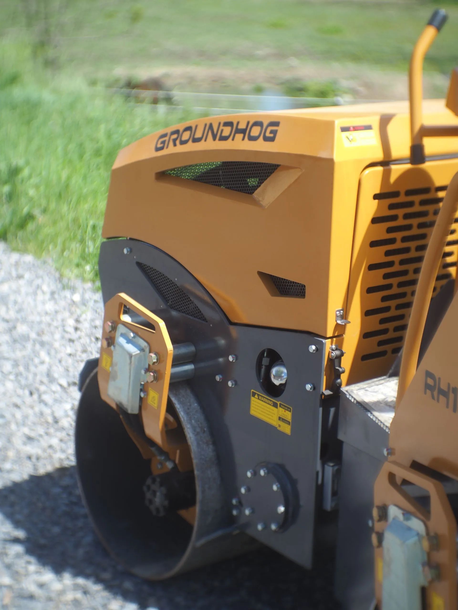A yellow Groundhog brand road roller sits on a gravel surface outdoors.