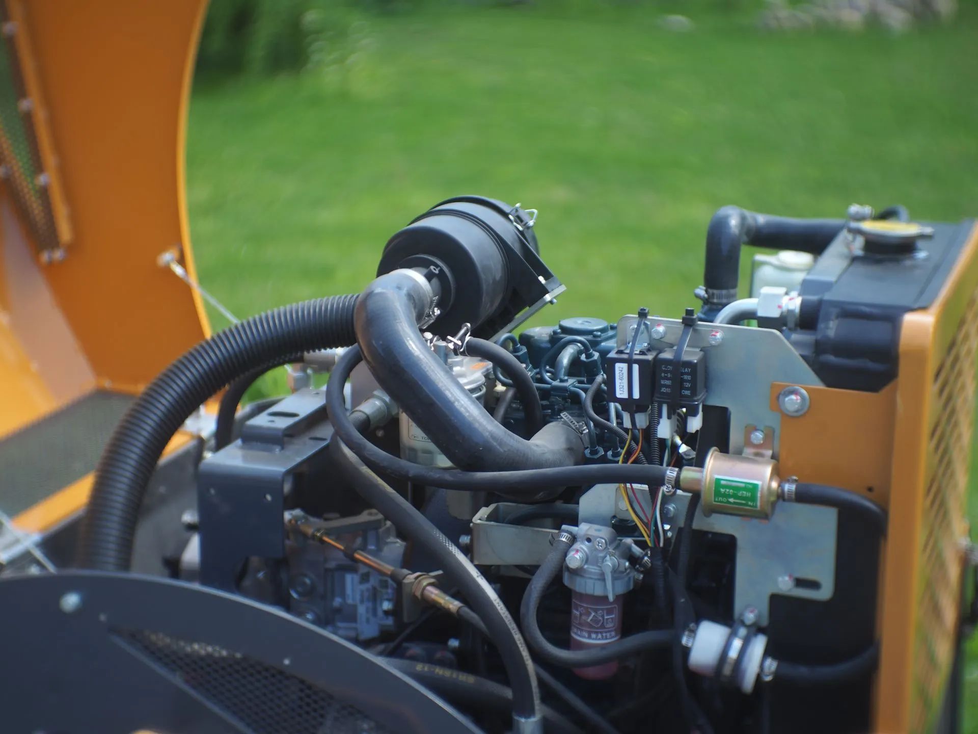 Open hood revealing the engine assembly of yellow industrial machinery, with hoses and filters visible outdoors.